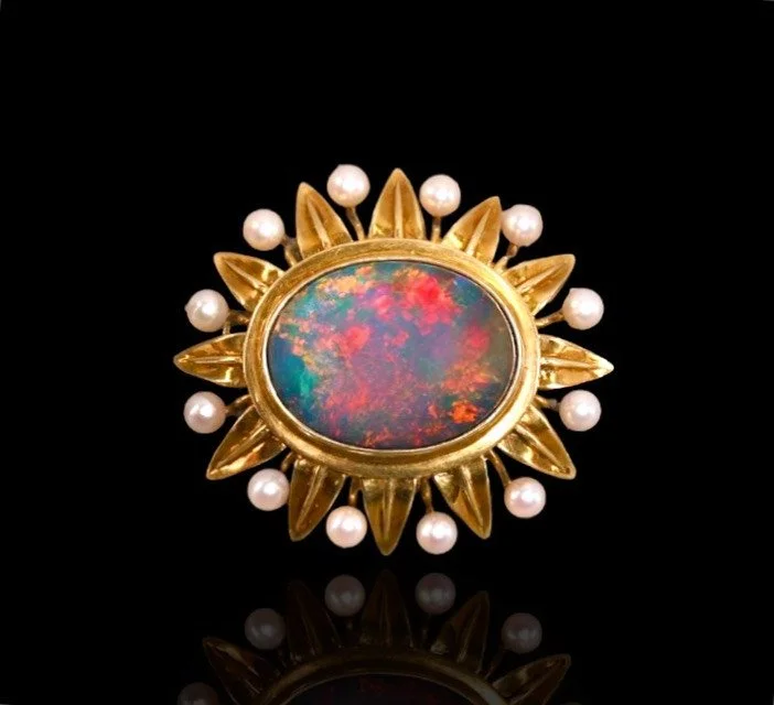 Broche ornée de diamants et de perles blanches, posée sur un fond orange.