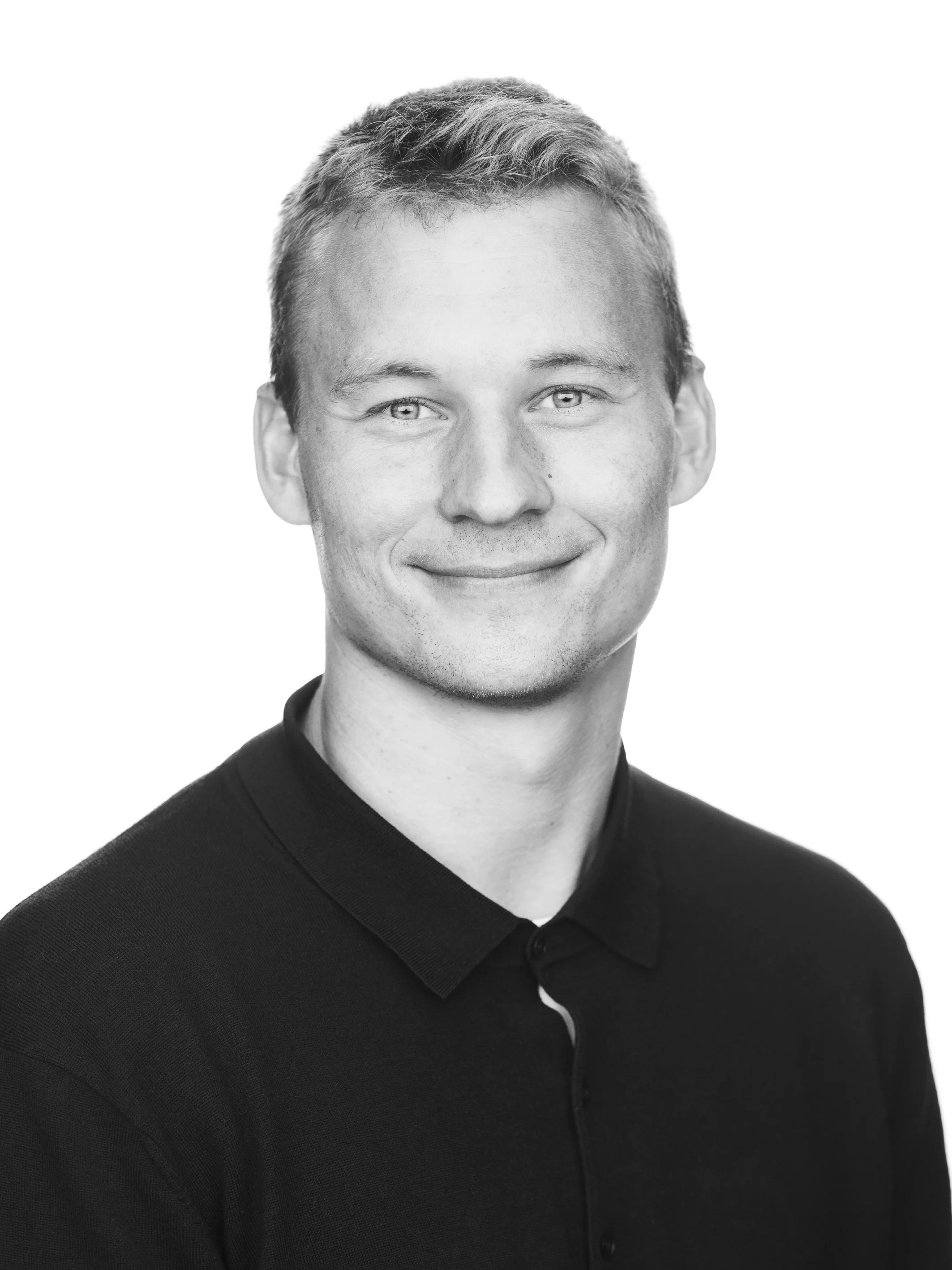 Black and white portrait of a young man with light hair, smiling, wearing a dark collared shirt.