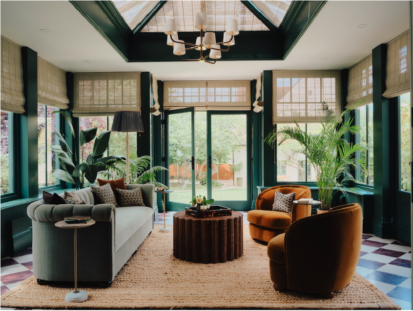 Imperfect Interiors designed orangery with large windows and doors painted in Imperfect Interiors x Pilgrim Nettle Tea paint. Contains a green sofa with cushions, two mustard coloured armchairs and indoor plants.