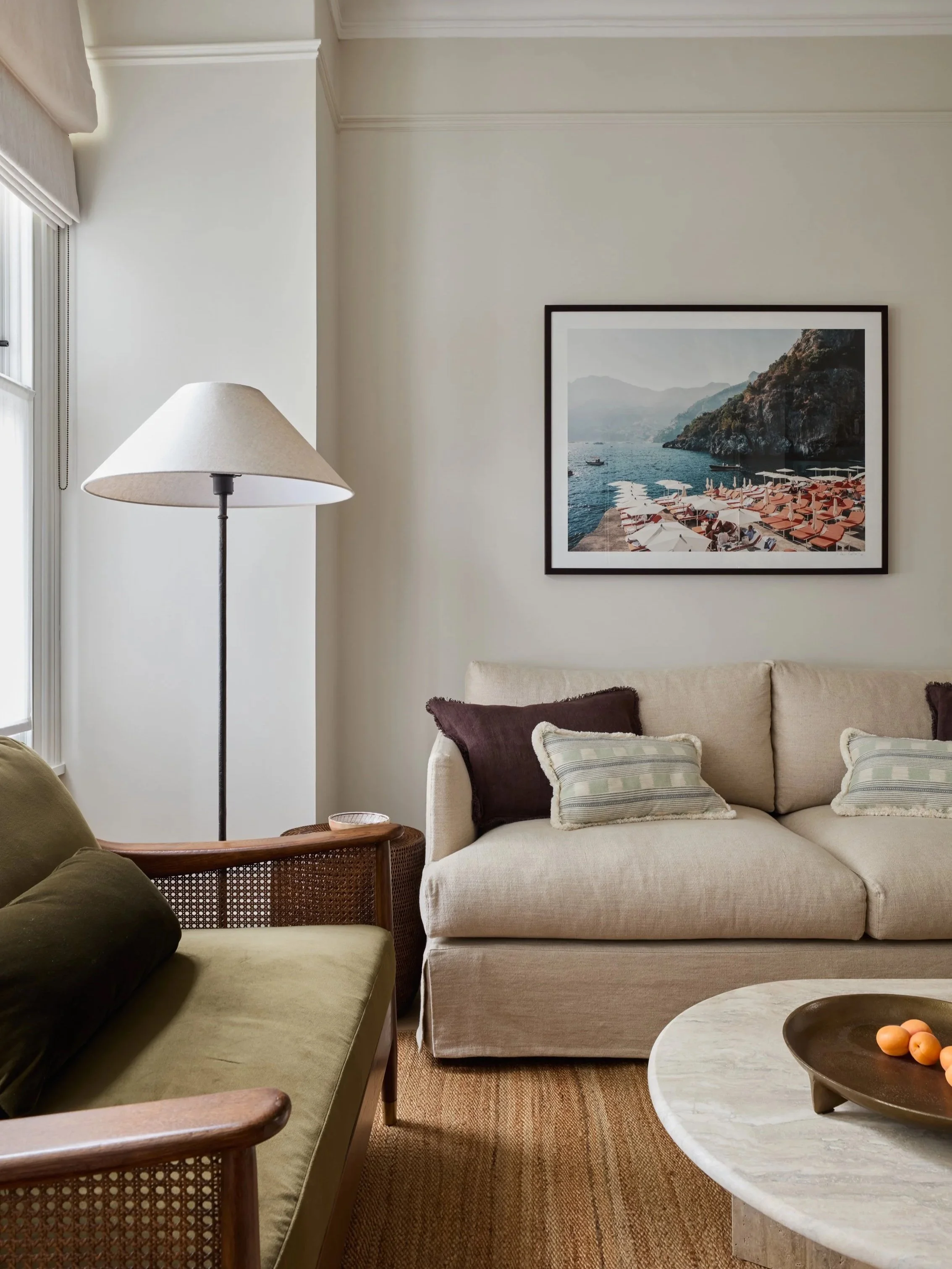 Imperfect Interiors designed ILiving room painted in Imperfect Interiors x Pilgrim Porridge,  with beige sofa, white and striped throw pillows, green armchair, wooden side table, white floor lamp, framed seascape photograph, round marble coffee table