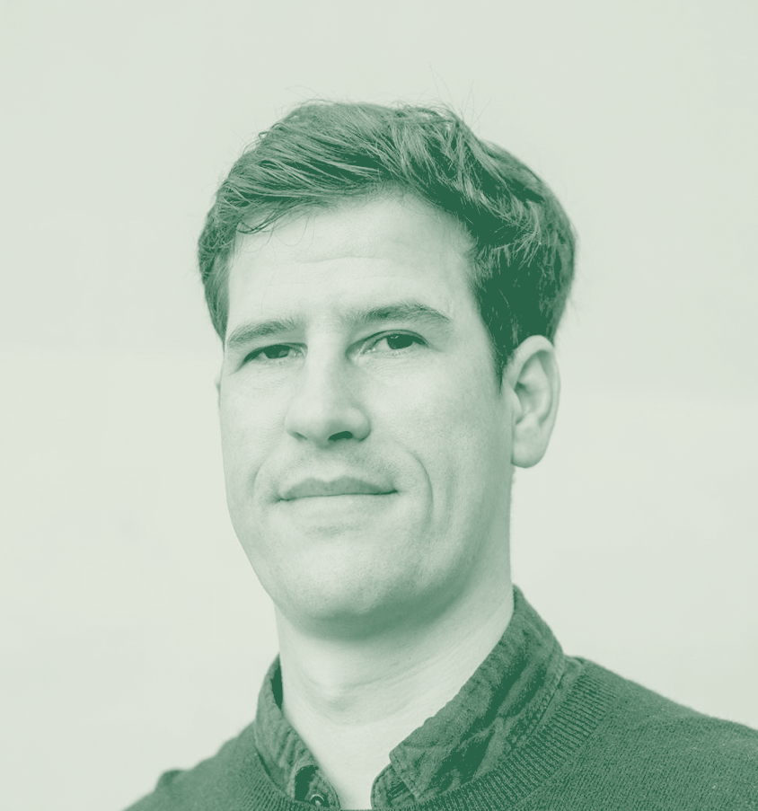 A portrait of a young man with short brown hair, wearing a dark sweater and a collared shirt, looking at the camera with a neutral expression.