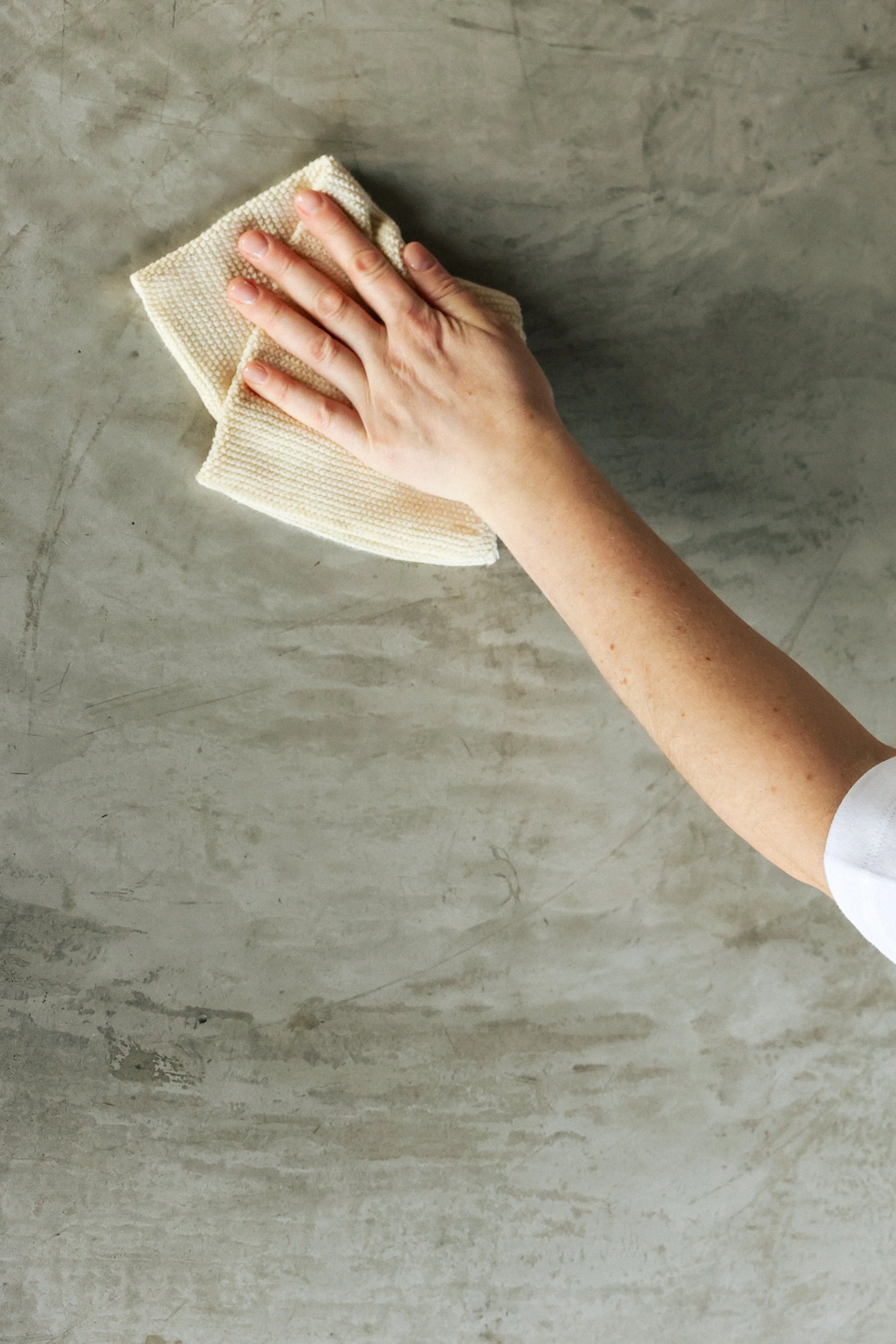 A person cleaning a gray concrete surface with a cream-colored cloth.