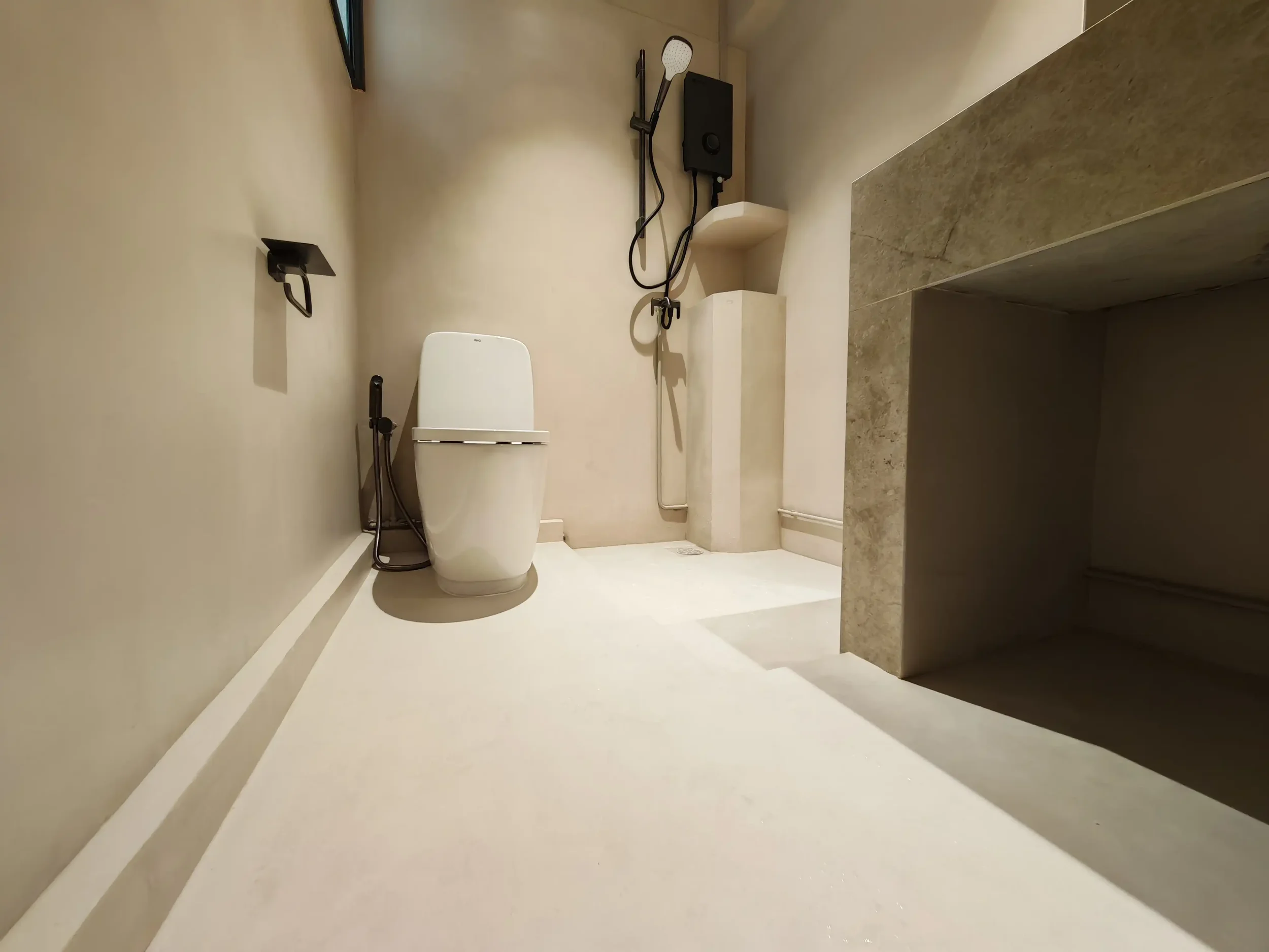 Singapore bathroom renovation with warm beige seamless microcement floor and wall finish, black fittings, white toilet and stone vanity.