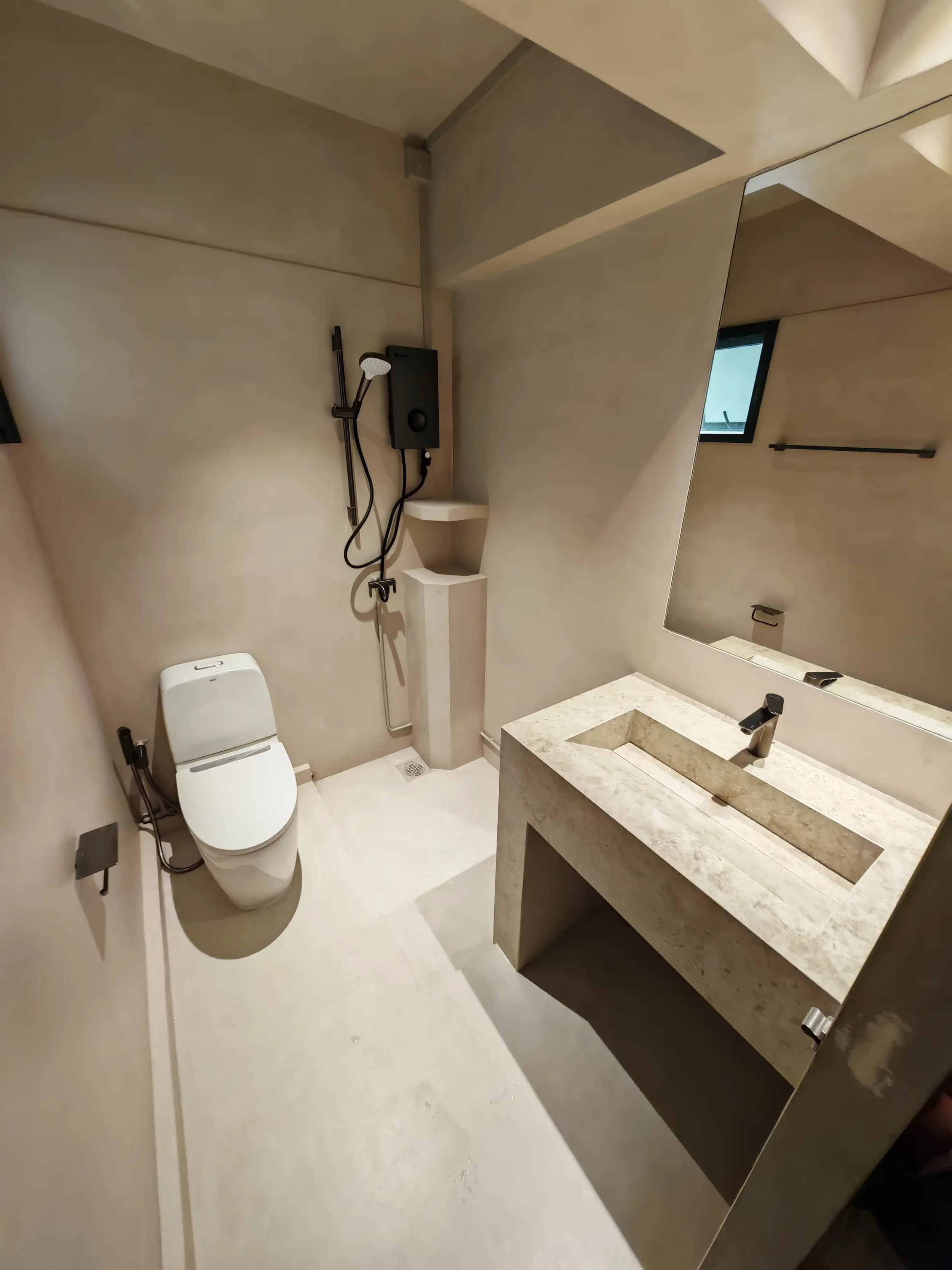 Singapore bathroom renovation project featuring Semiforêt microcement finishes across the floor and wall surfaces. The warm beige mineral texture creates a seamless, calm and cohesive wet-area atmosphere, paired with black fittings, white sanitary wa