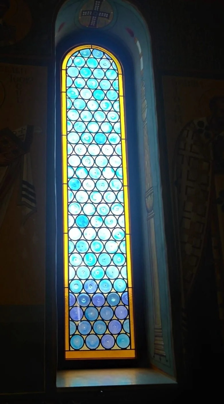Colorful stained glass window with blue, yellow, and purple circular patterns in a church.