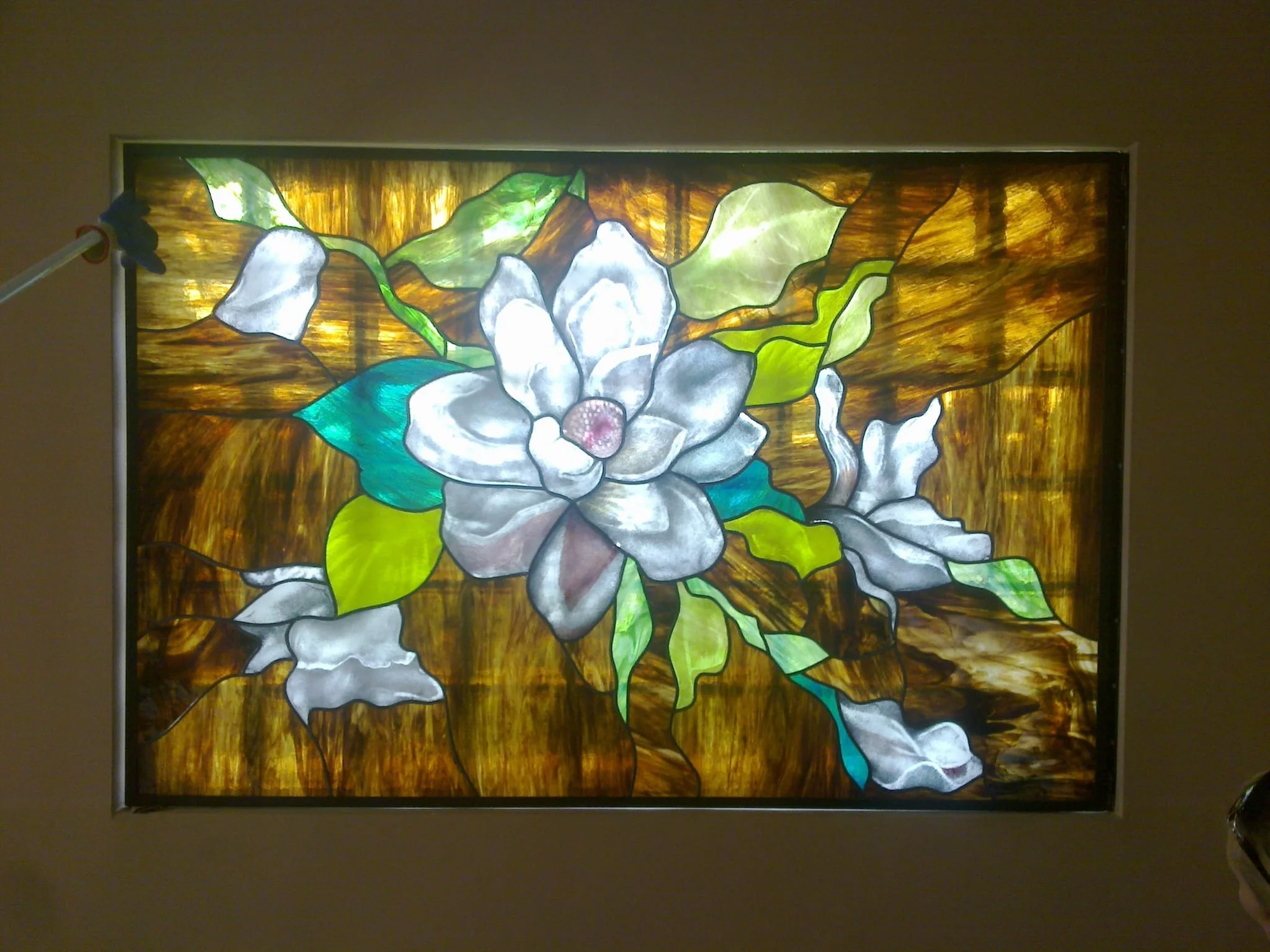 Colorful stained glass window featuring a white flower with green leaves against a background of amber and brown hues.