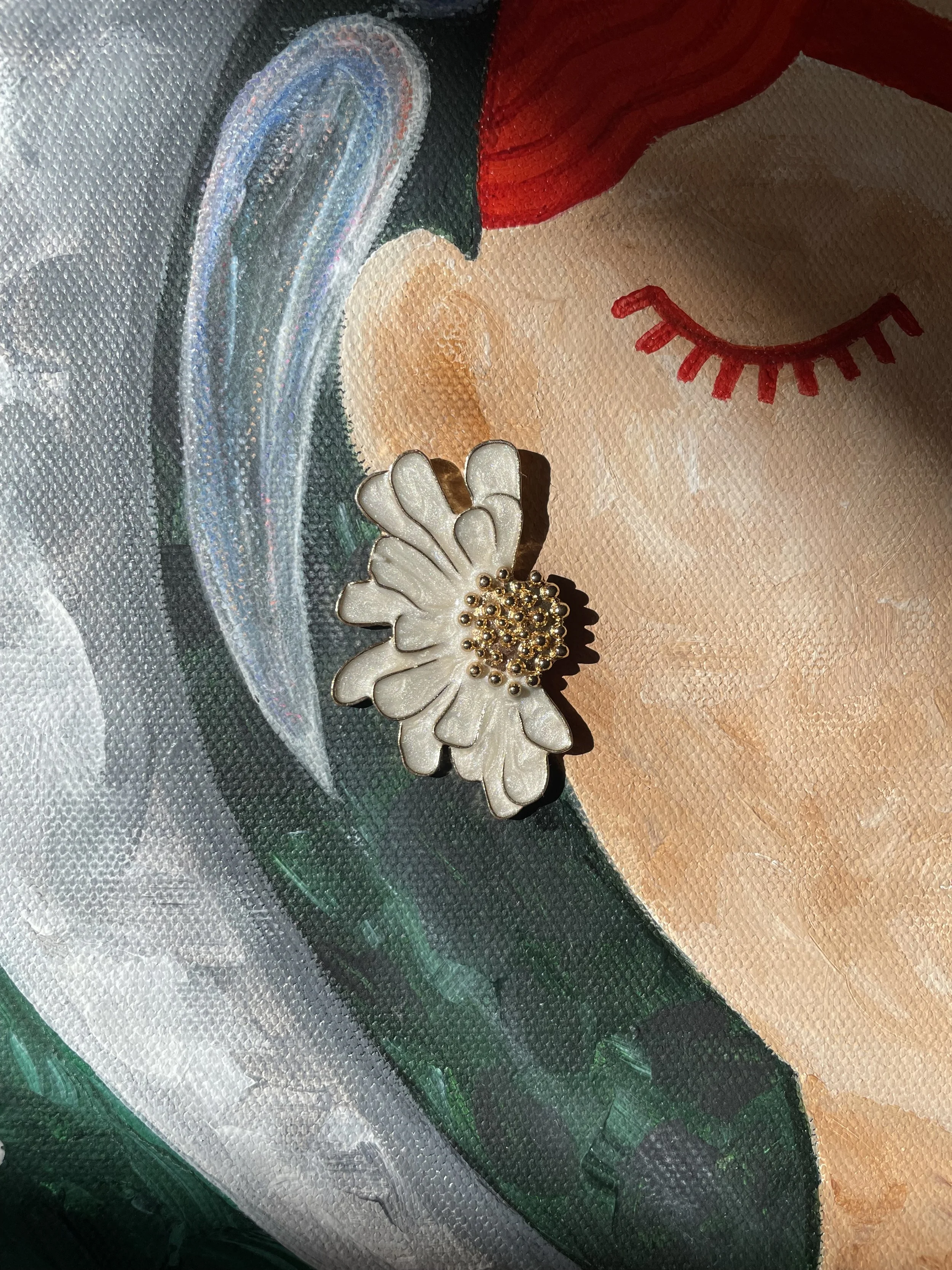 Detail of a female astronaut painting featuring bright red hair, closed eyes, and delicate white daisy earrings with gold centers.