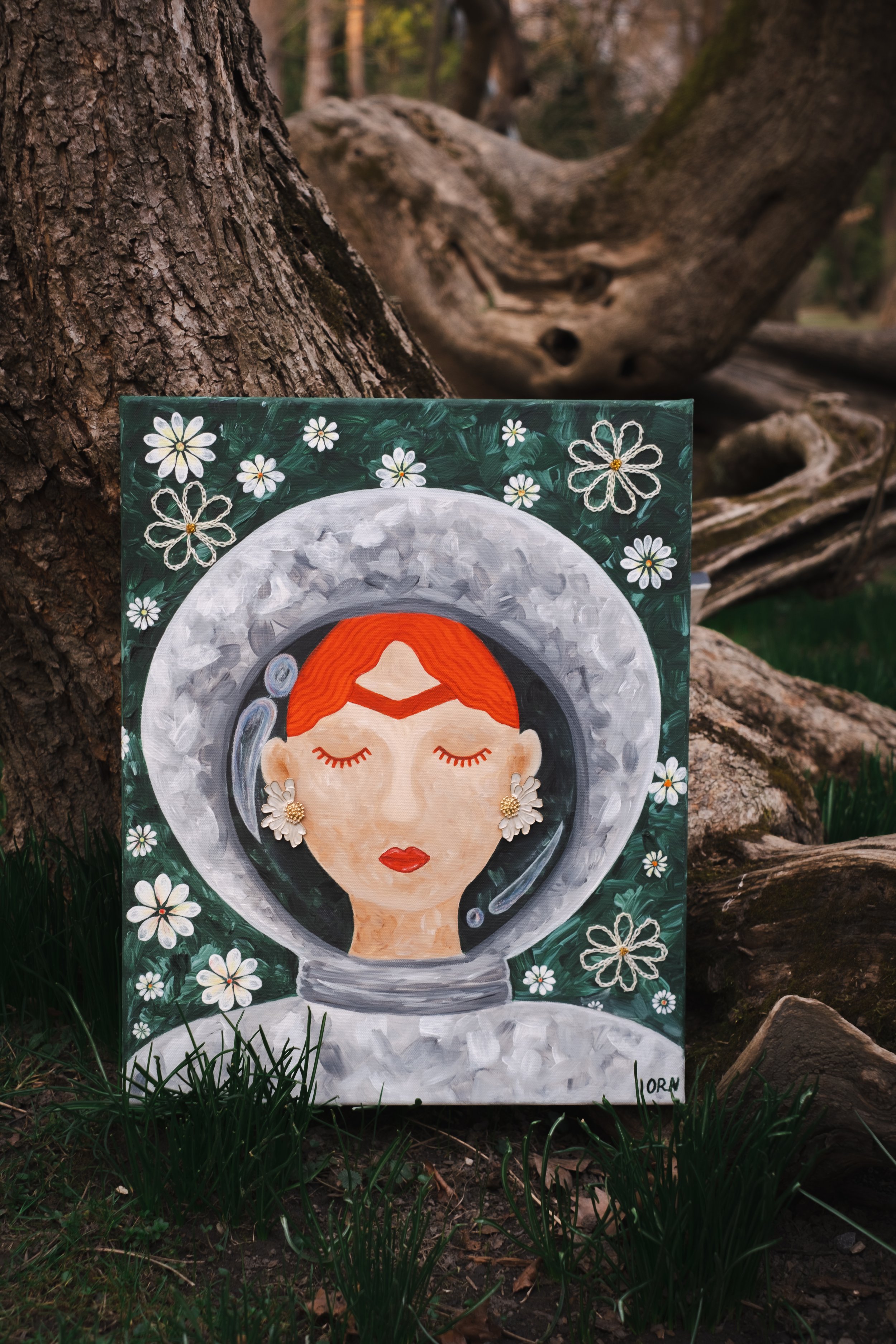 Space Frida painting by Oleksandra Roche-Newton placed against a textured tree trunk in a park, depicting a female astronaut in a daisy-filled galaxy.
