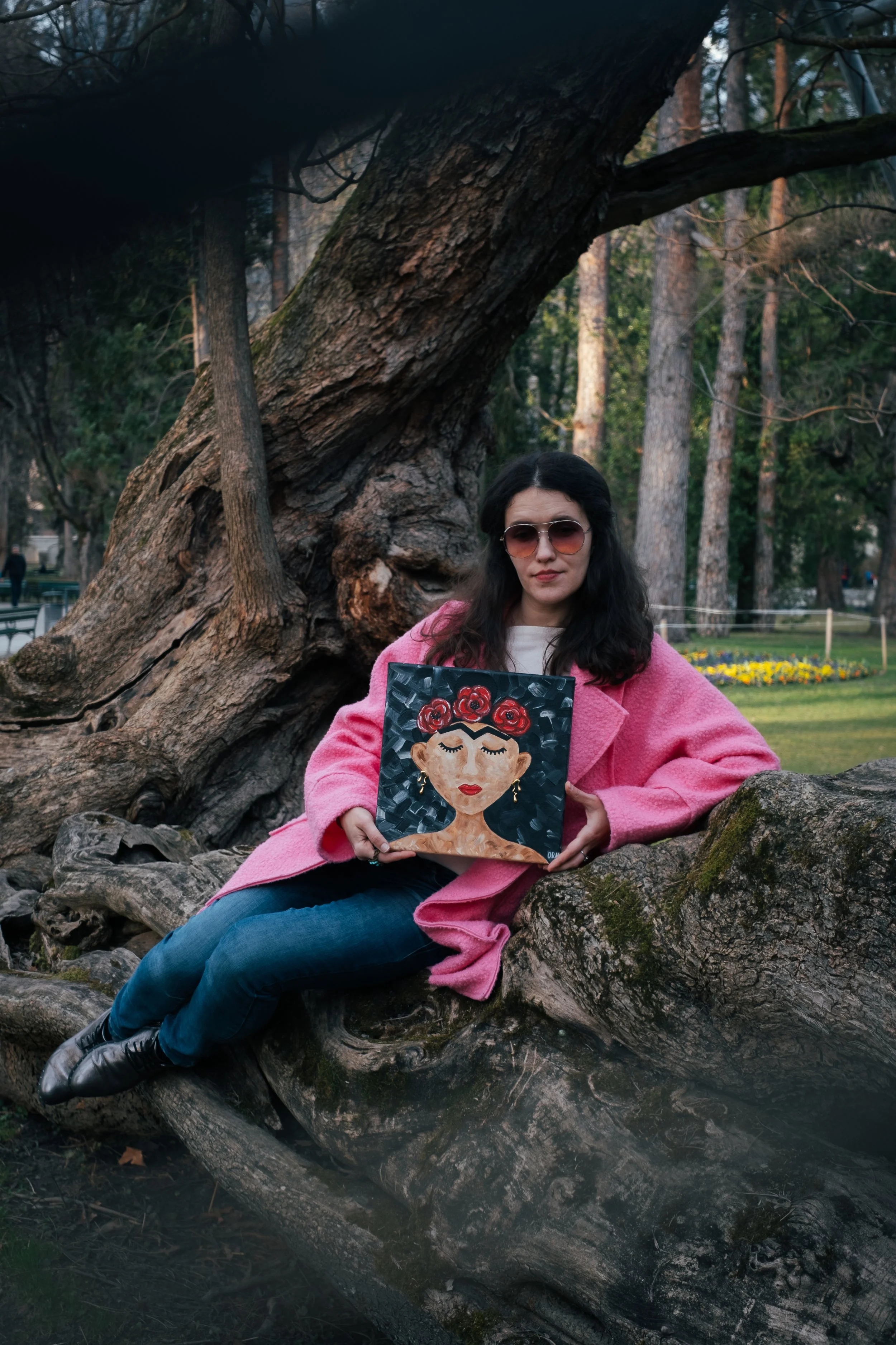 Artist Oleksandra Roche-Newton presents her 2025 work, "Frida with Poppies." This lifestyle photo shows the square canvas in a natural outdoor setting, highlighting the vibrant red poppies and the painting's size relative to the artist.