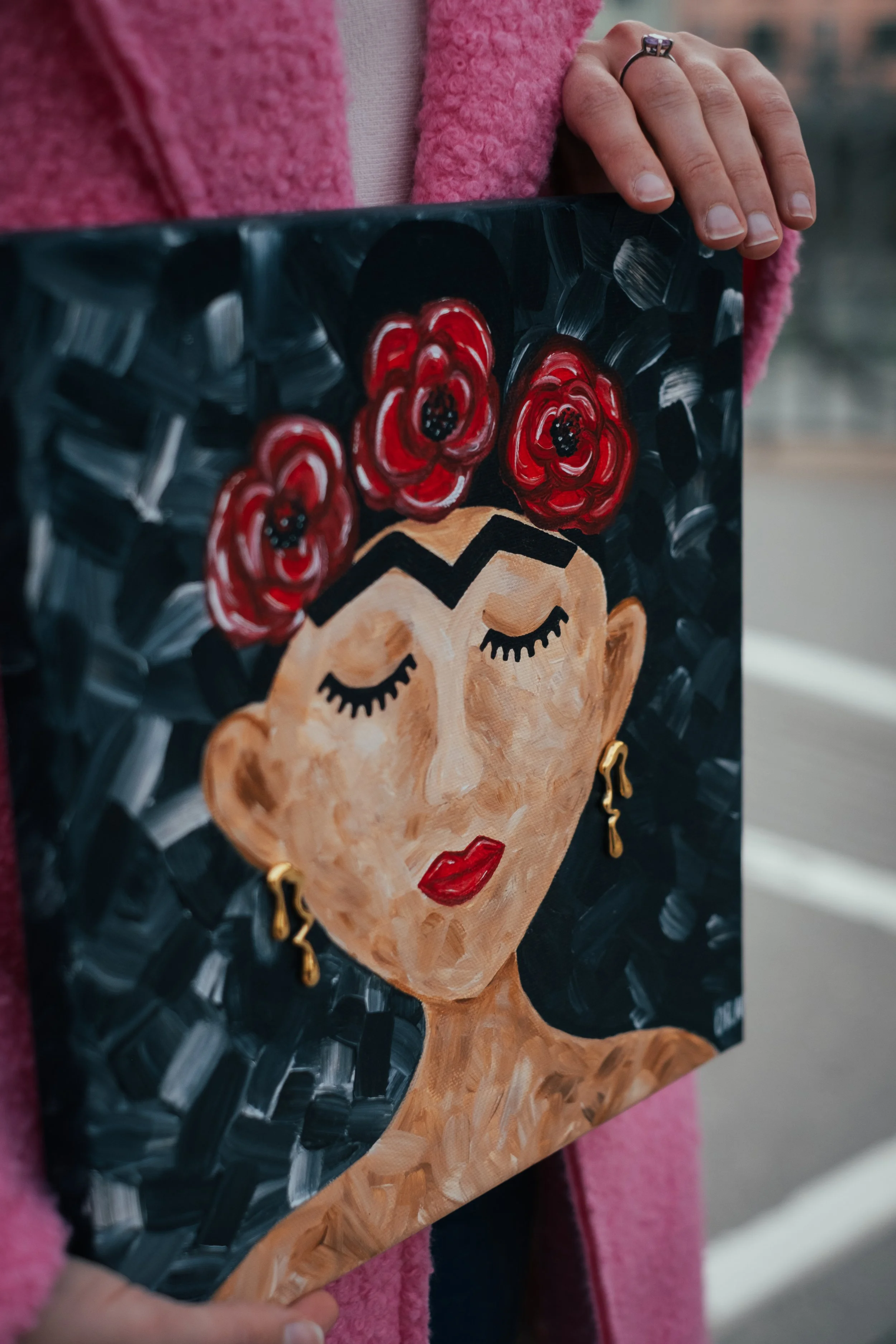 A detailed view highlighting the intricate textile work integrated into the canvas. Artist Oleksandra Roche-Newton uses red poppies to show her love to flowers and their meaning in Frida’s hair, complete with detailed black beaded centers, alongside 