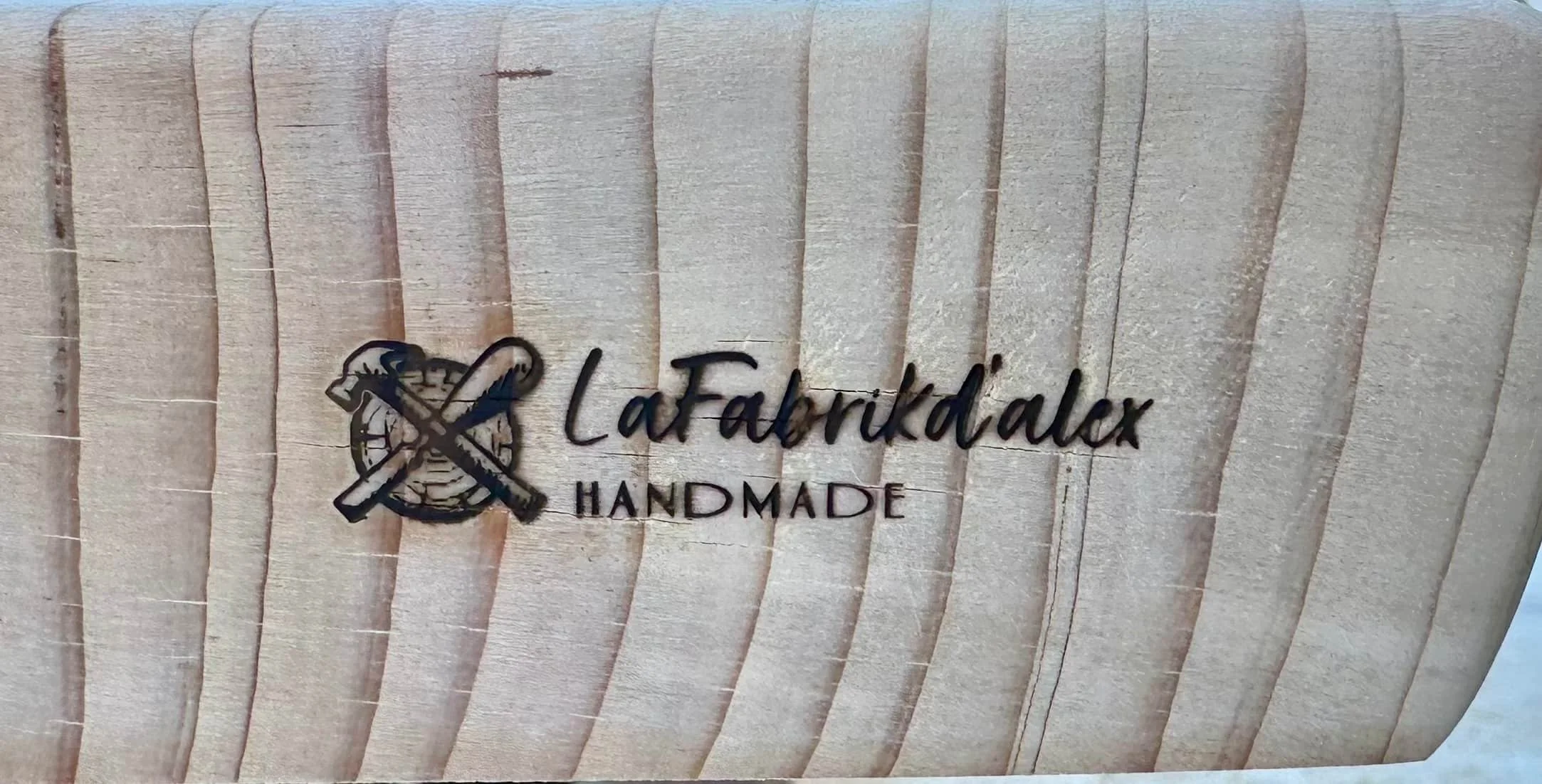 Une planche de bois avec une inscription en verre noir : La Fabrikd'alex  HANDMADE.