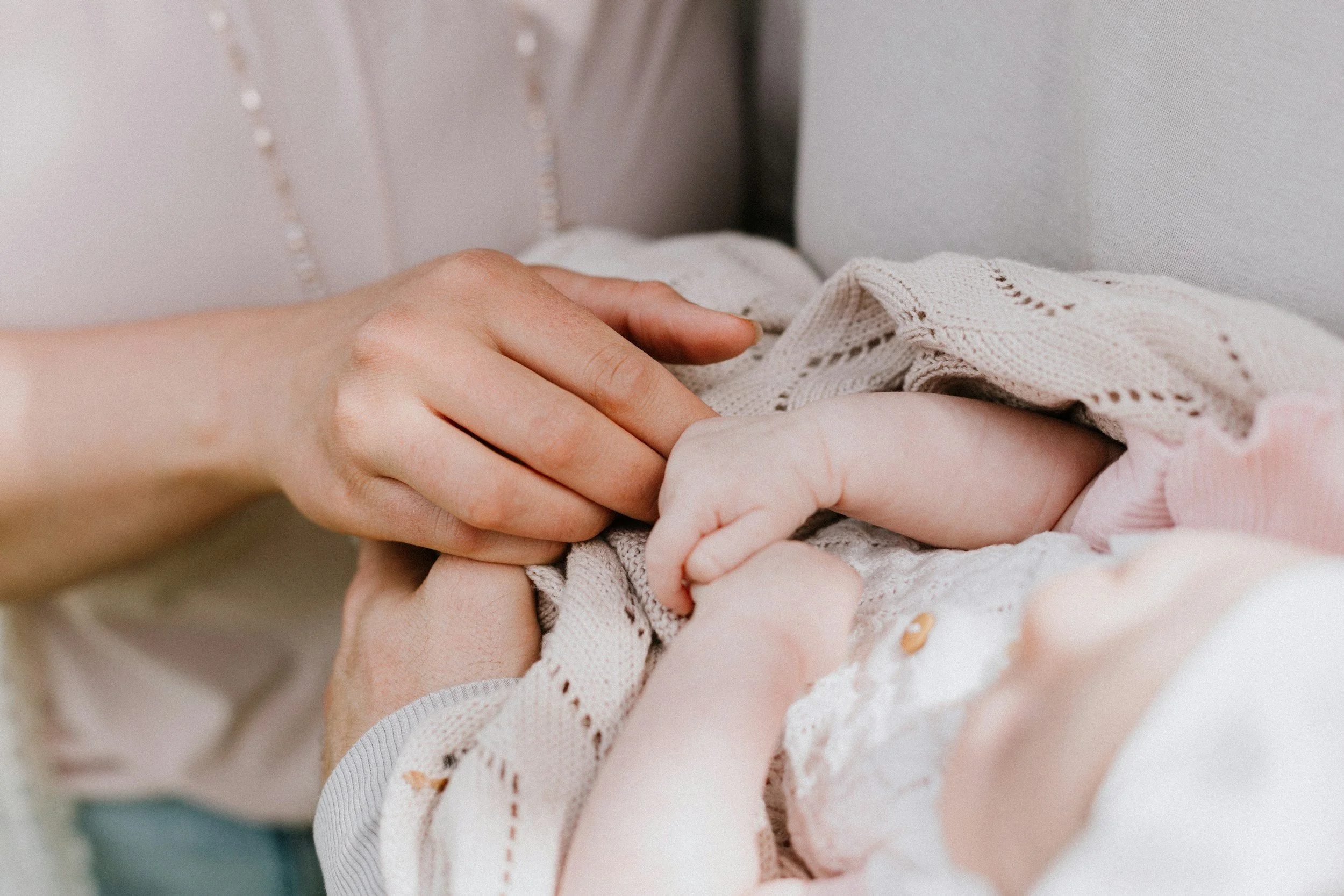 Close-up of an adult's and a baby's hands holding each other, with the adult gently holding the baby's hand.