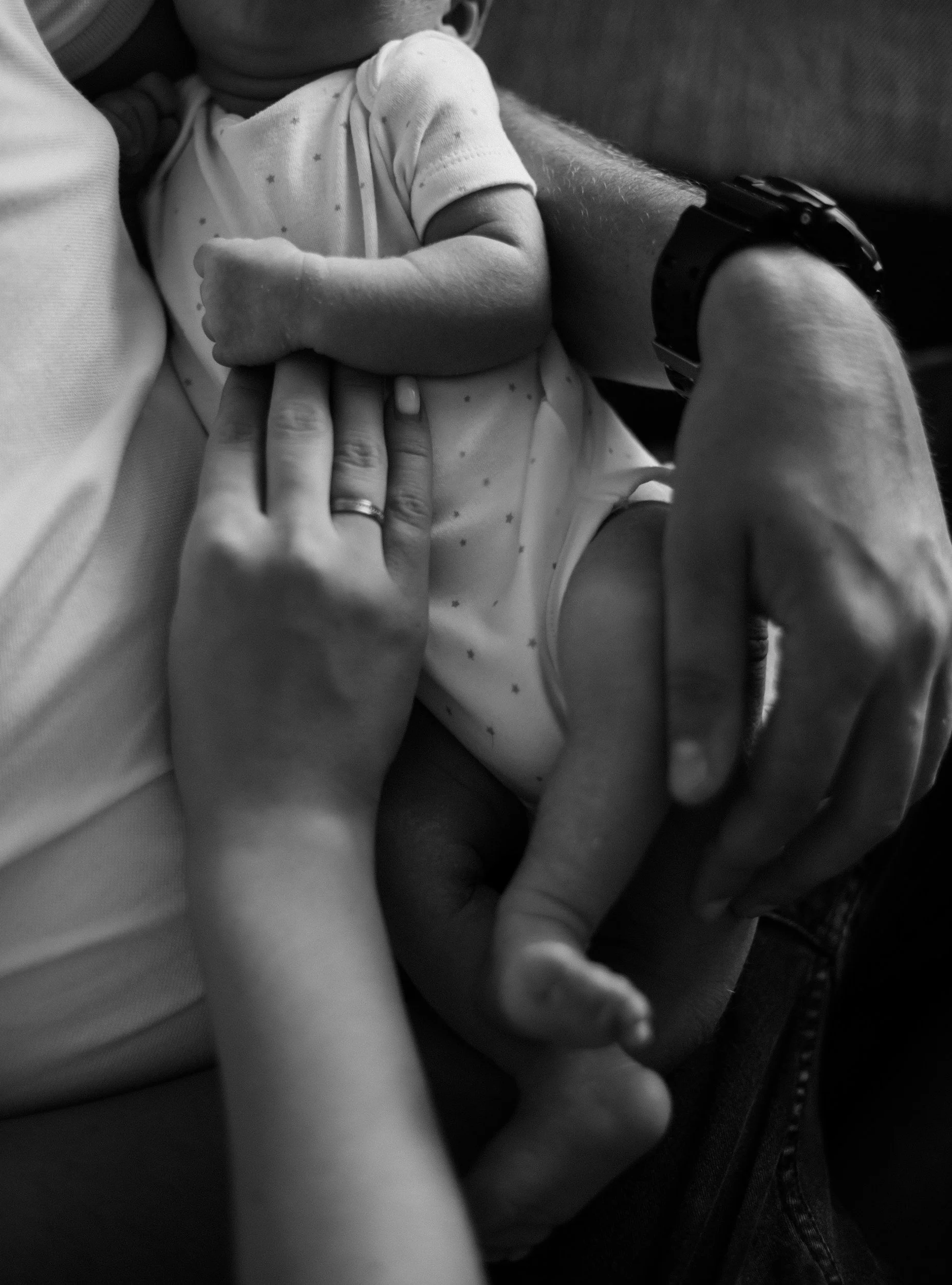 Adult cradling a newborn baby, both hands touching, black and white photo.