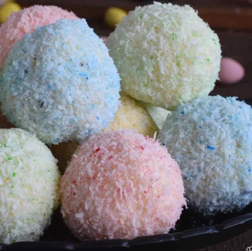 Colorful coconut-covered candies or confections in pastel shades of pink, blue, green, and yellow, arranged on a dark platter.