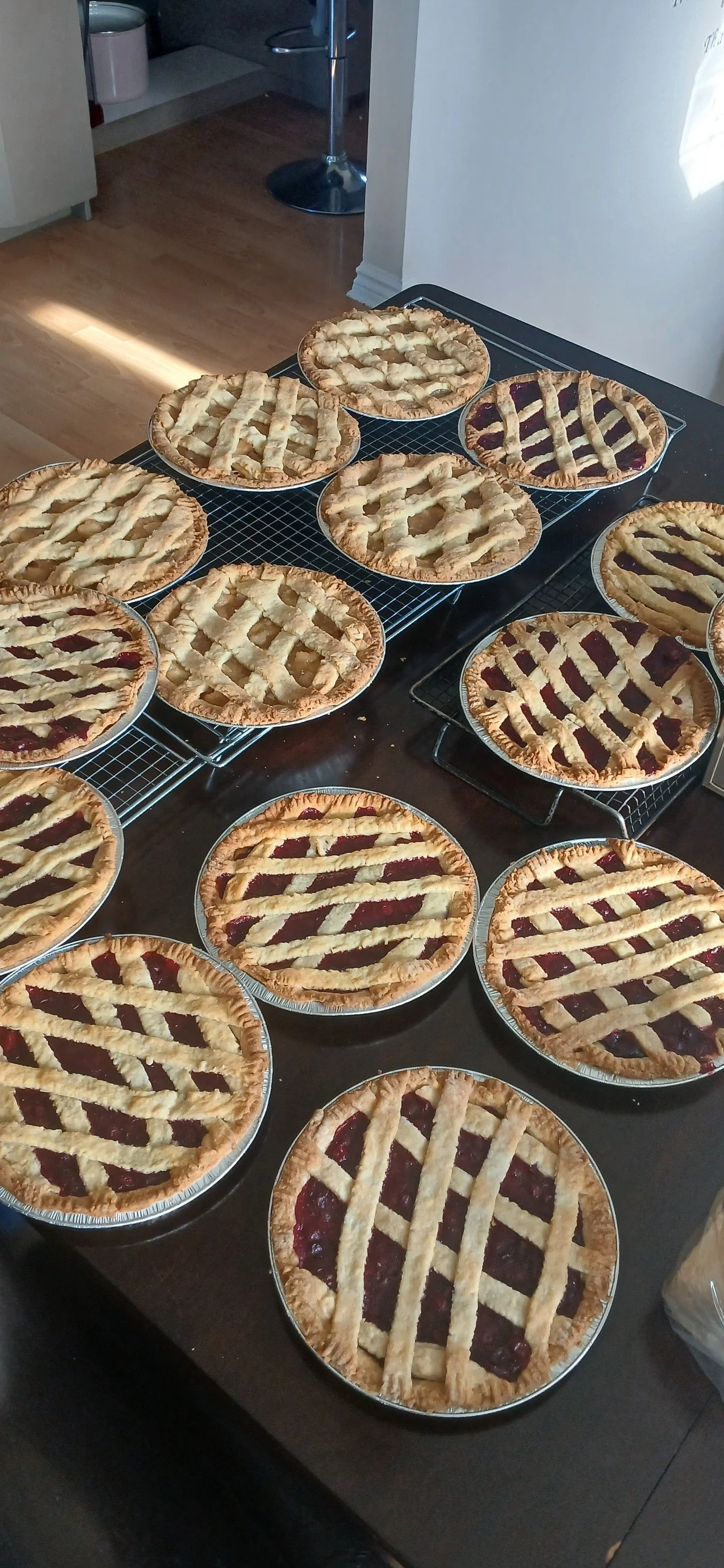 Several homemade cherry pies with lattice crusts cooling on wire racks and a countertop.