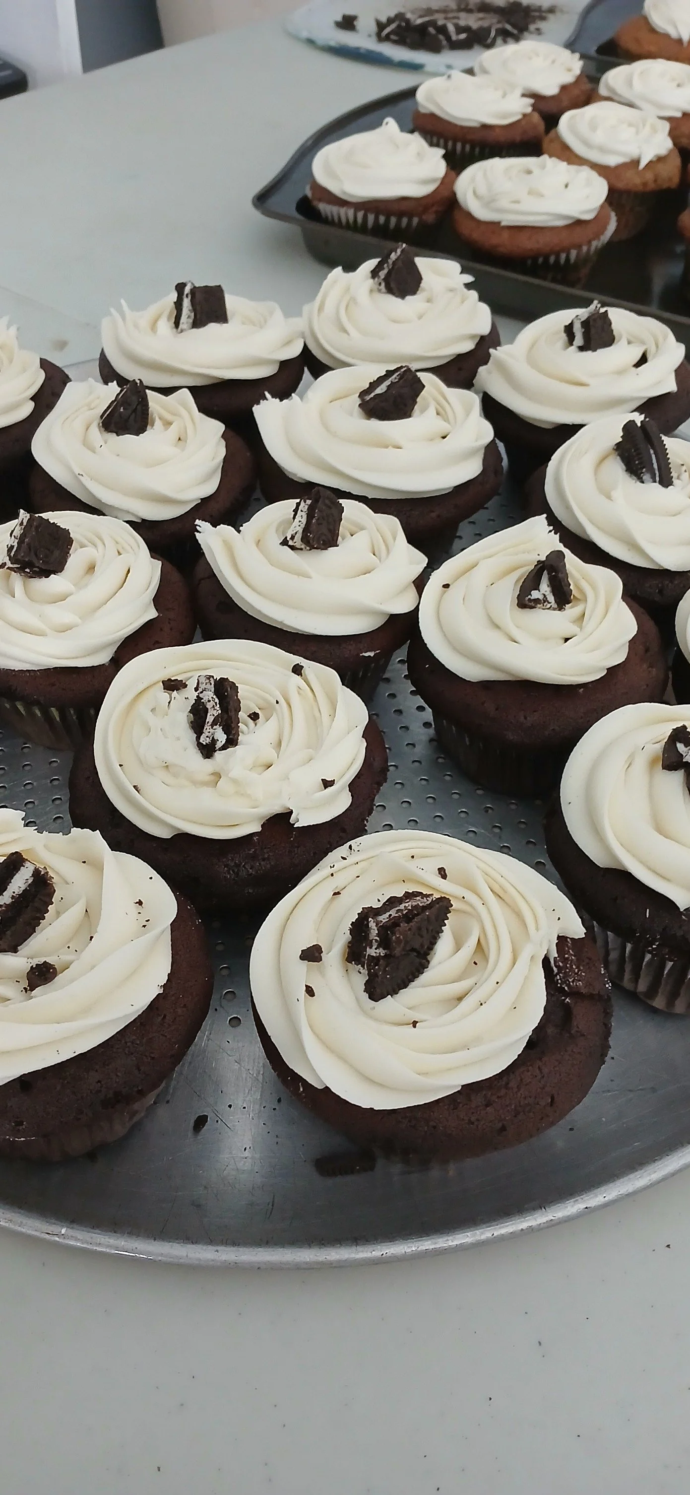 Chocolate cupcakes topped with white icing and Oreo cookie pieces on a metal tray.