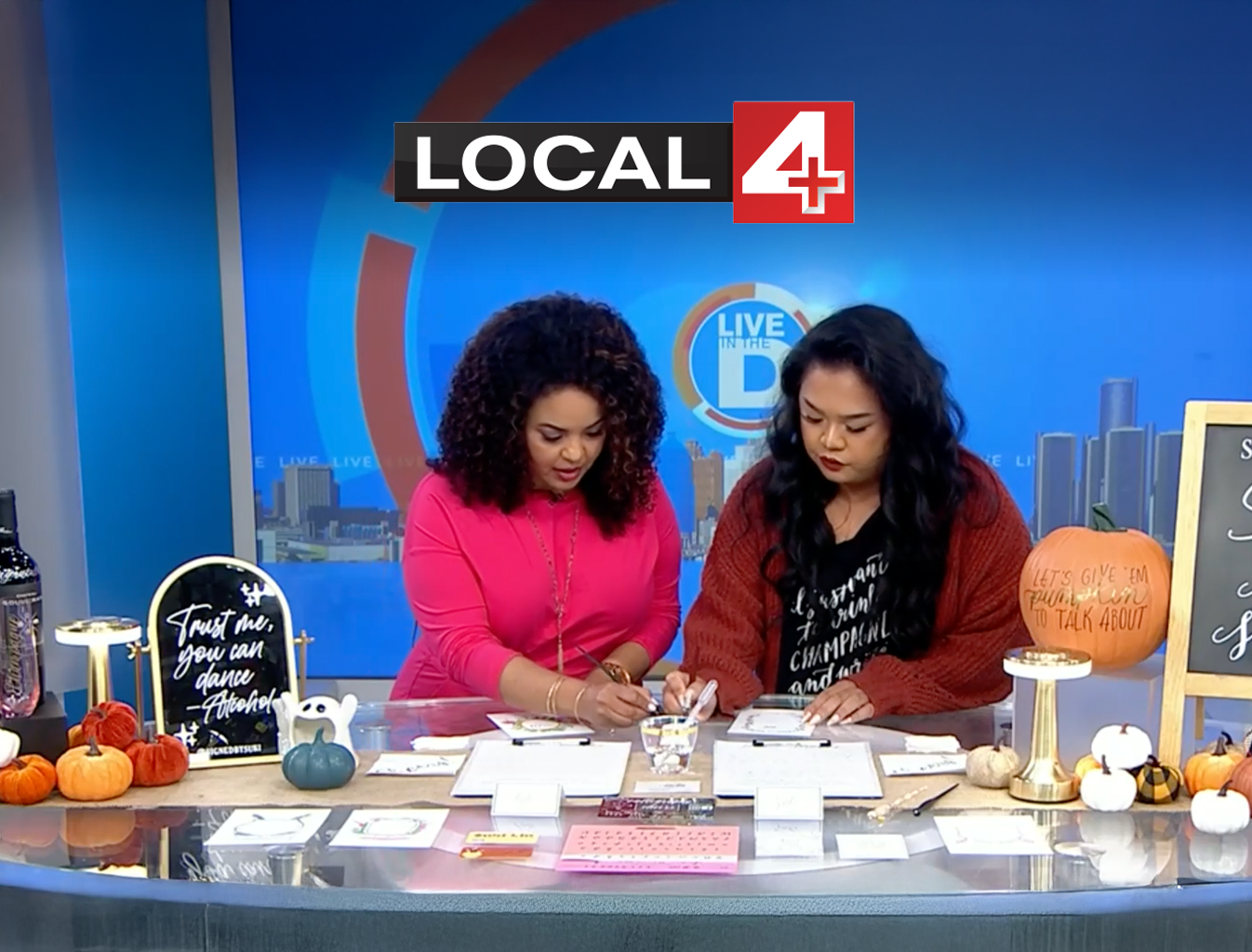 Two women on a news show testing out calligraphy materials with a Local 4 logo over top