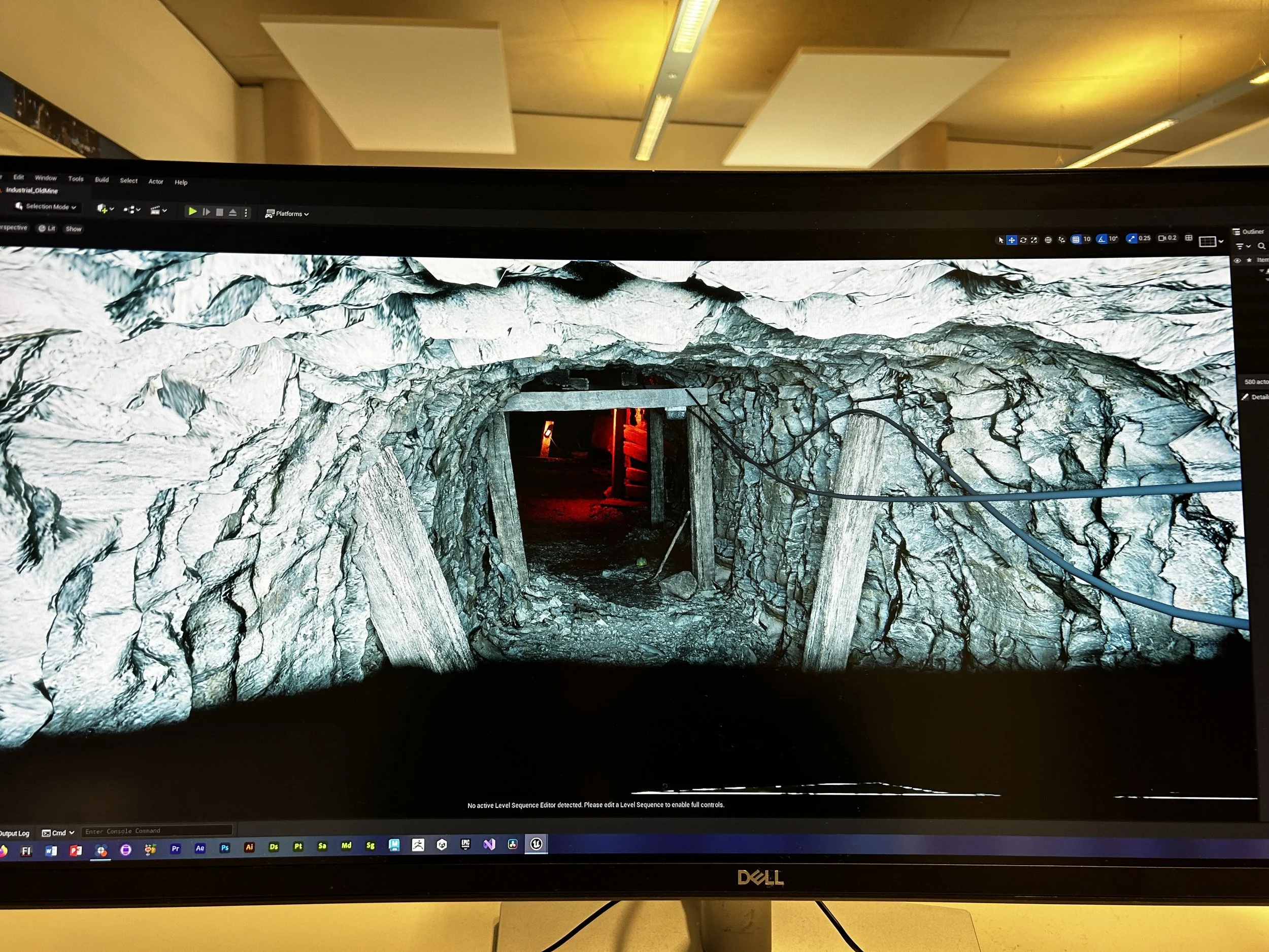 A computer screen showing a digital 3D rendering of an underground tunnel with rocky walls, supported by wooden beams, with some electrical cables.