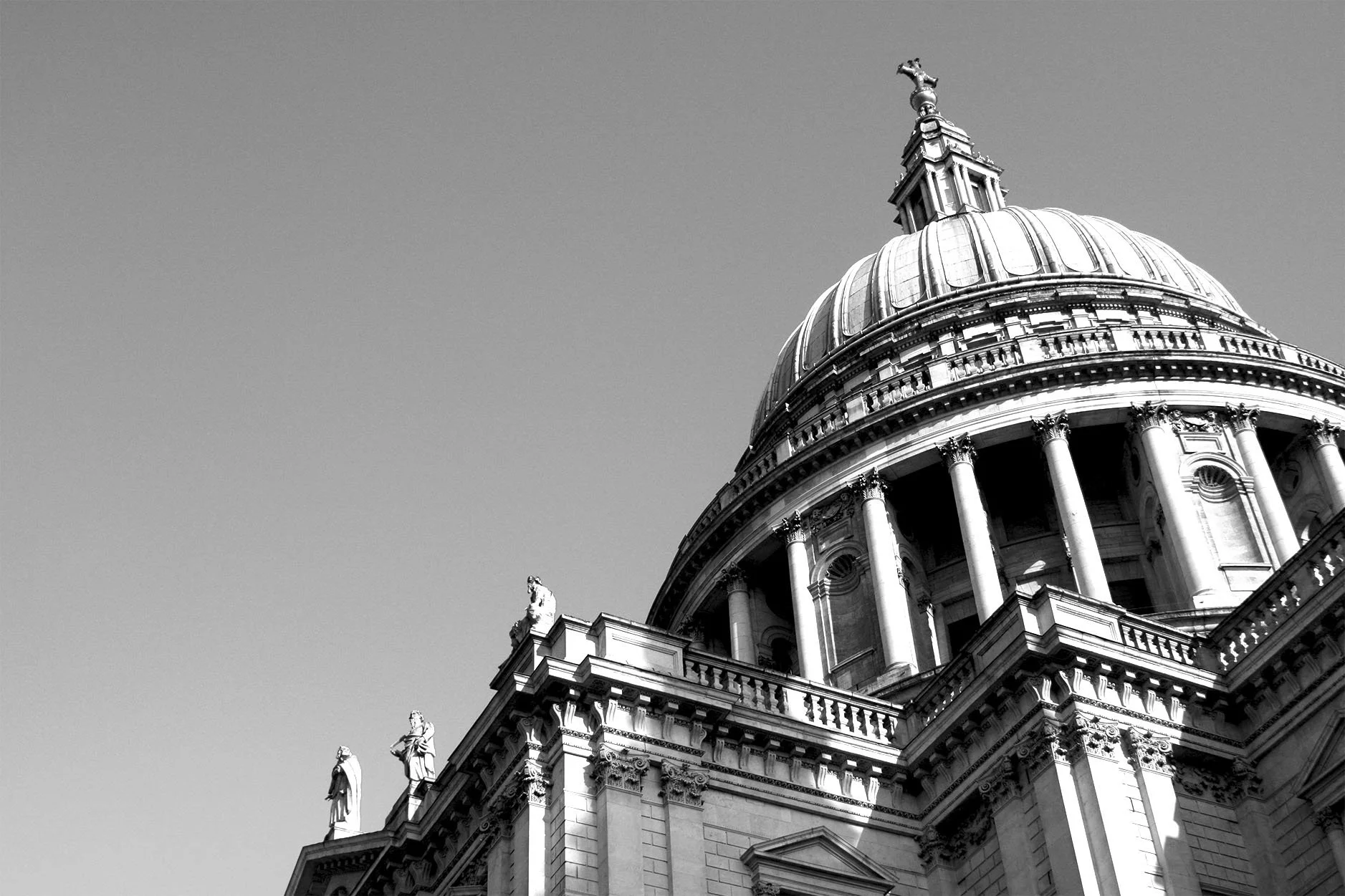 Black and white photo of the domed St. Peter's Basilica in Vatican City, with statues along the rooftop and a clear sky background.