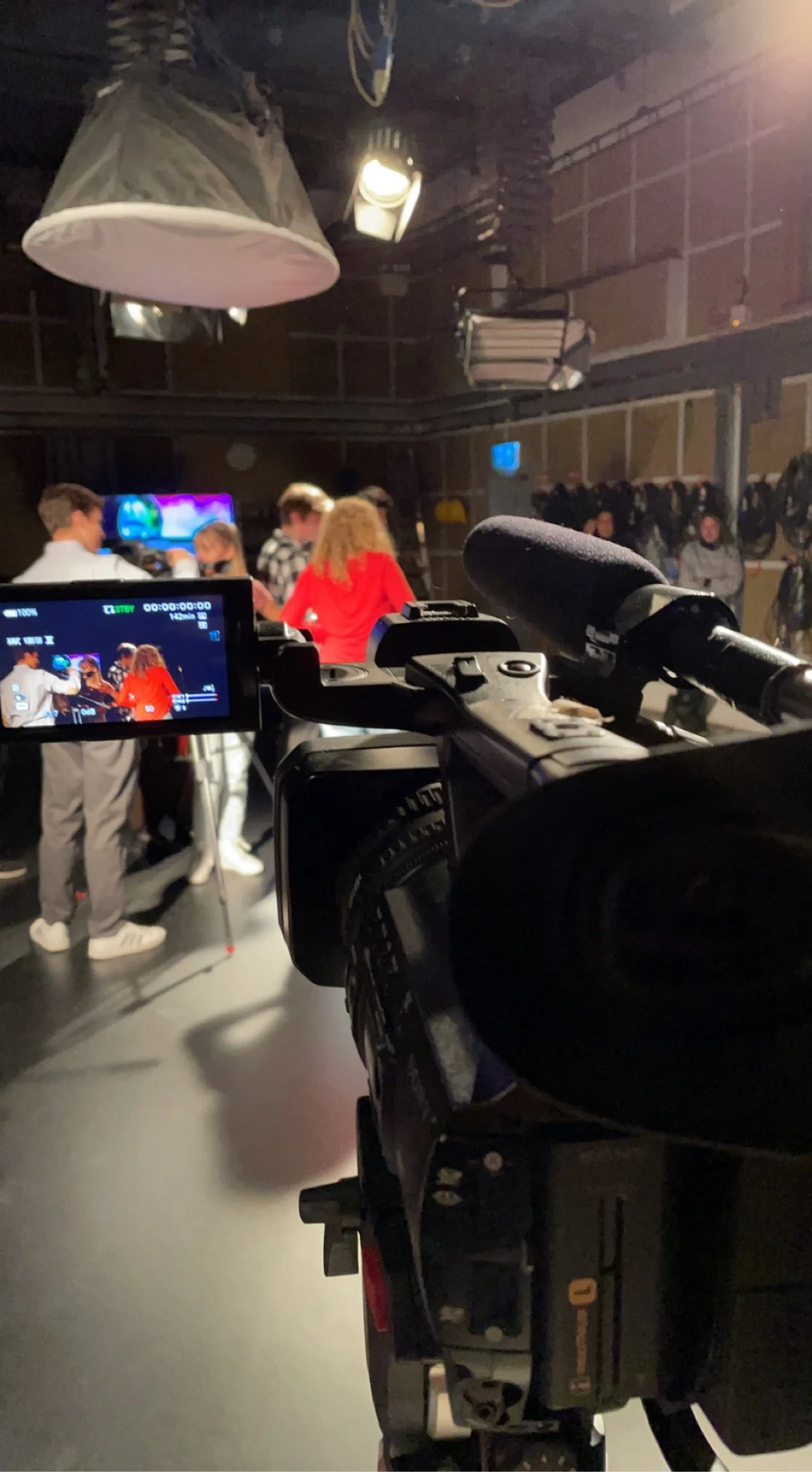 Video camera filming a group of young people in a studio with professional lighting and a backdrop.