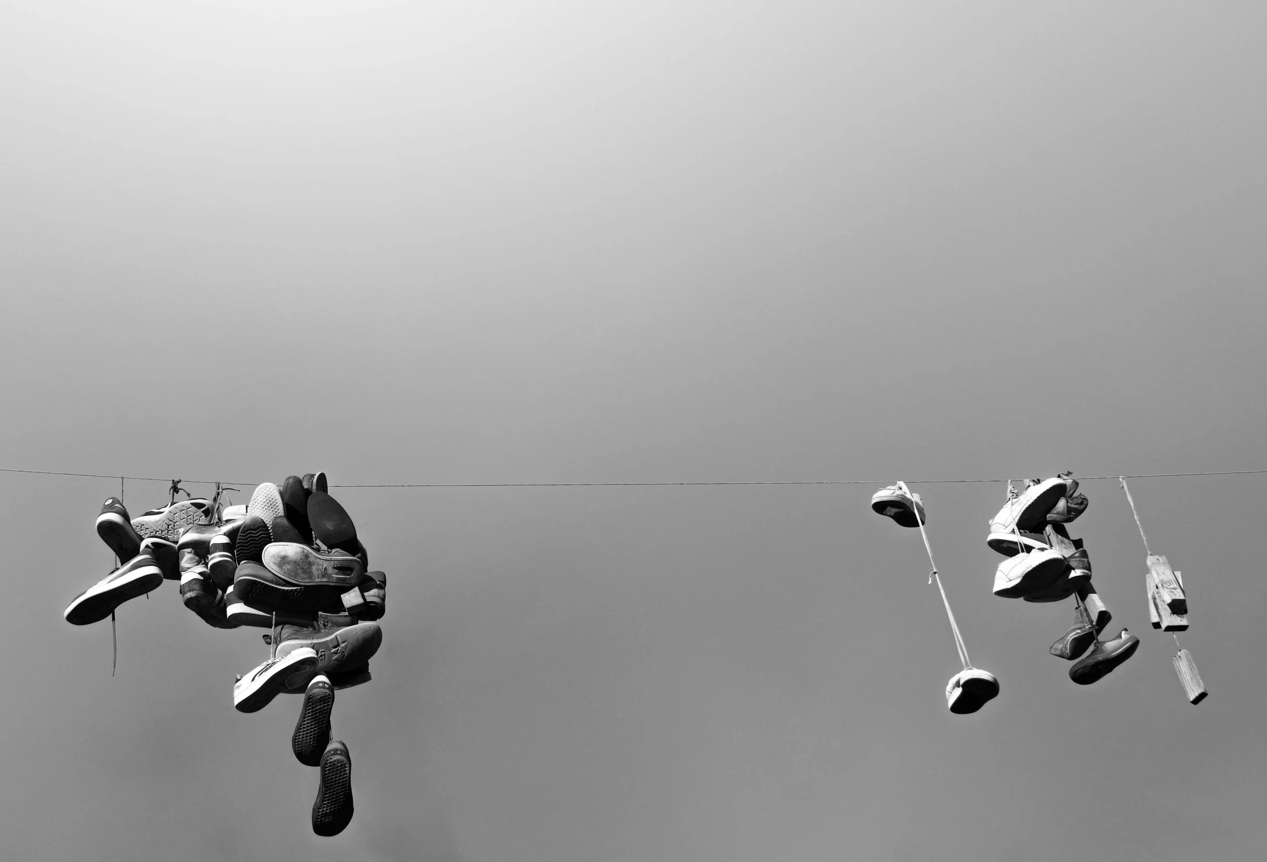 Clotheslines with shoes hanging on them against a gray sky.