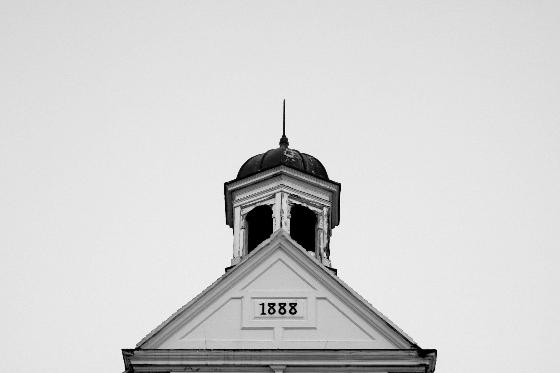 The top of a building with a weathered bell tower and the year 1888 on the front in black numbers, black and white photo.