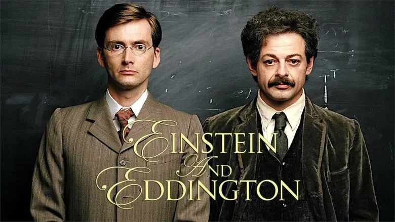 Photo of two men dressed as scientists, standing in front of a blackboard with writing. The image features the title 'Einstein and Eddington' in elegant gold script.