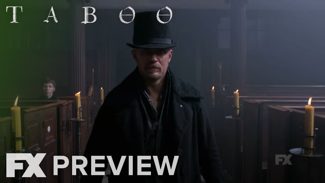 A man in a black coat and top hat standing in a dimly lit church with candles along the pews. A woman is visible in the background.