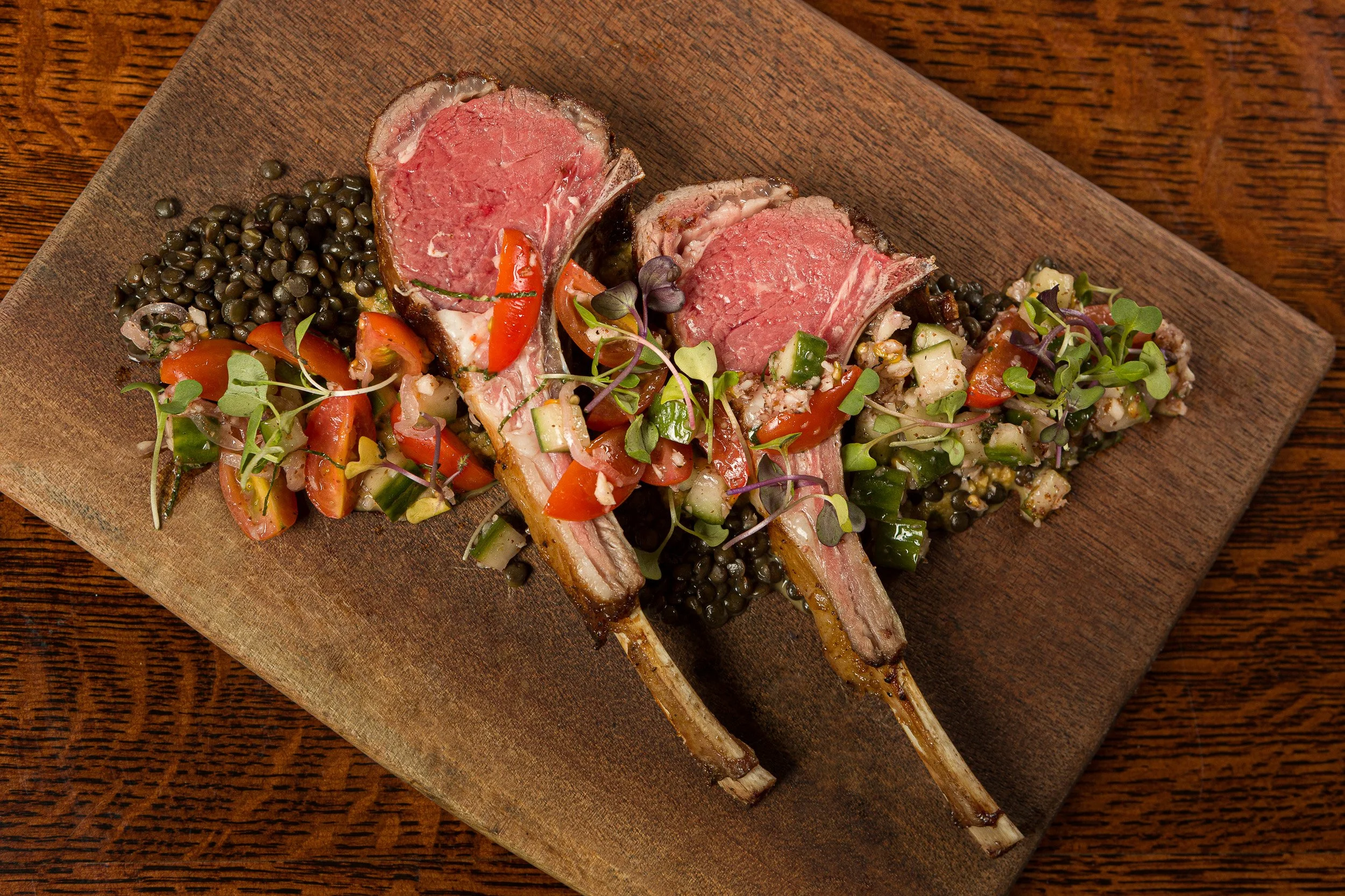 Grilled lamb chops with a mixed vegetable salad and black beans on a wooden platter.