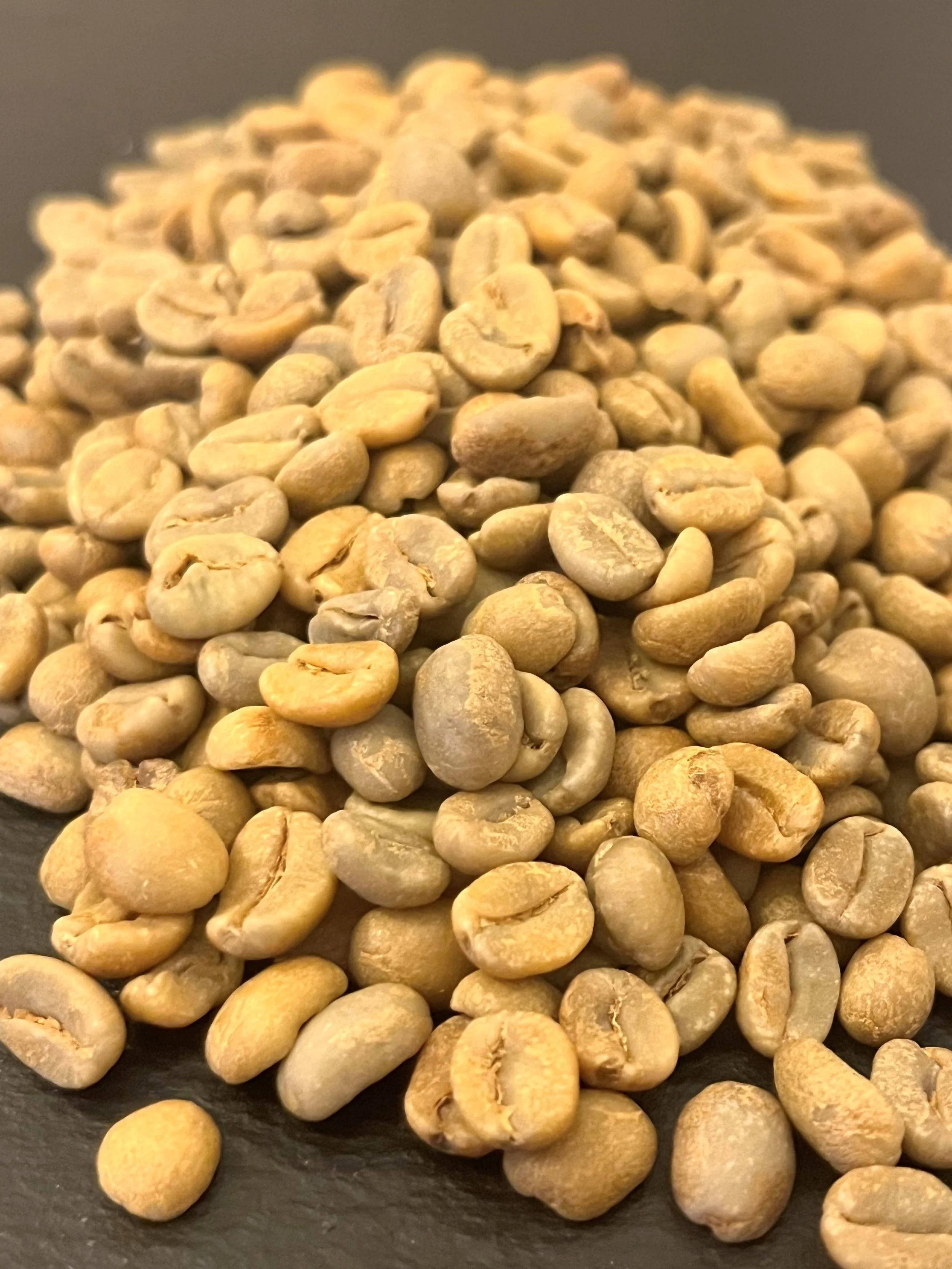 Close-up of unroasted green coffee beans on a dark surface.