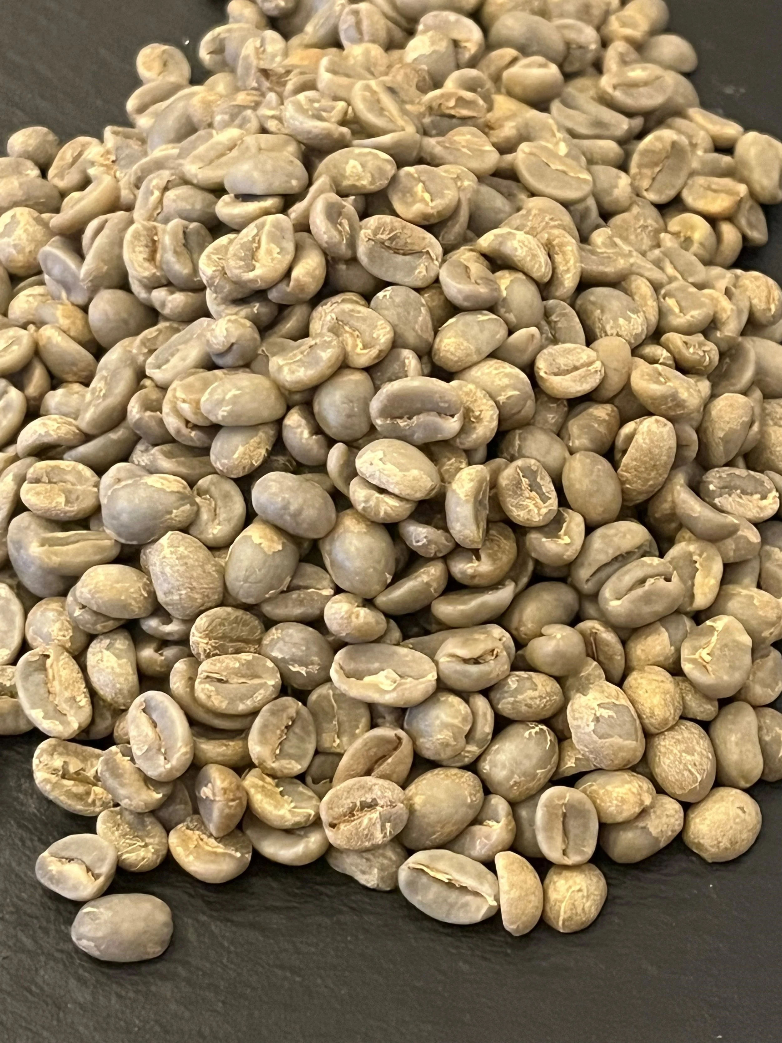 Close-up of green coffee beans on a black surface.