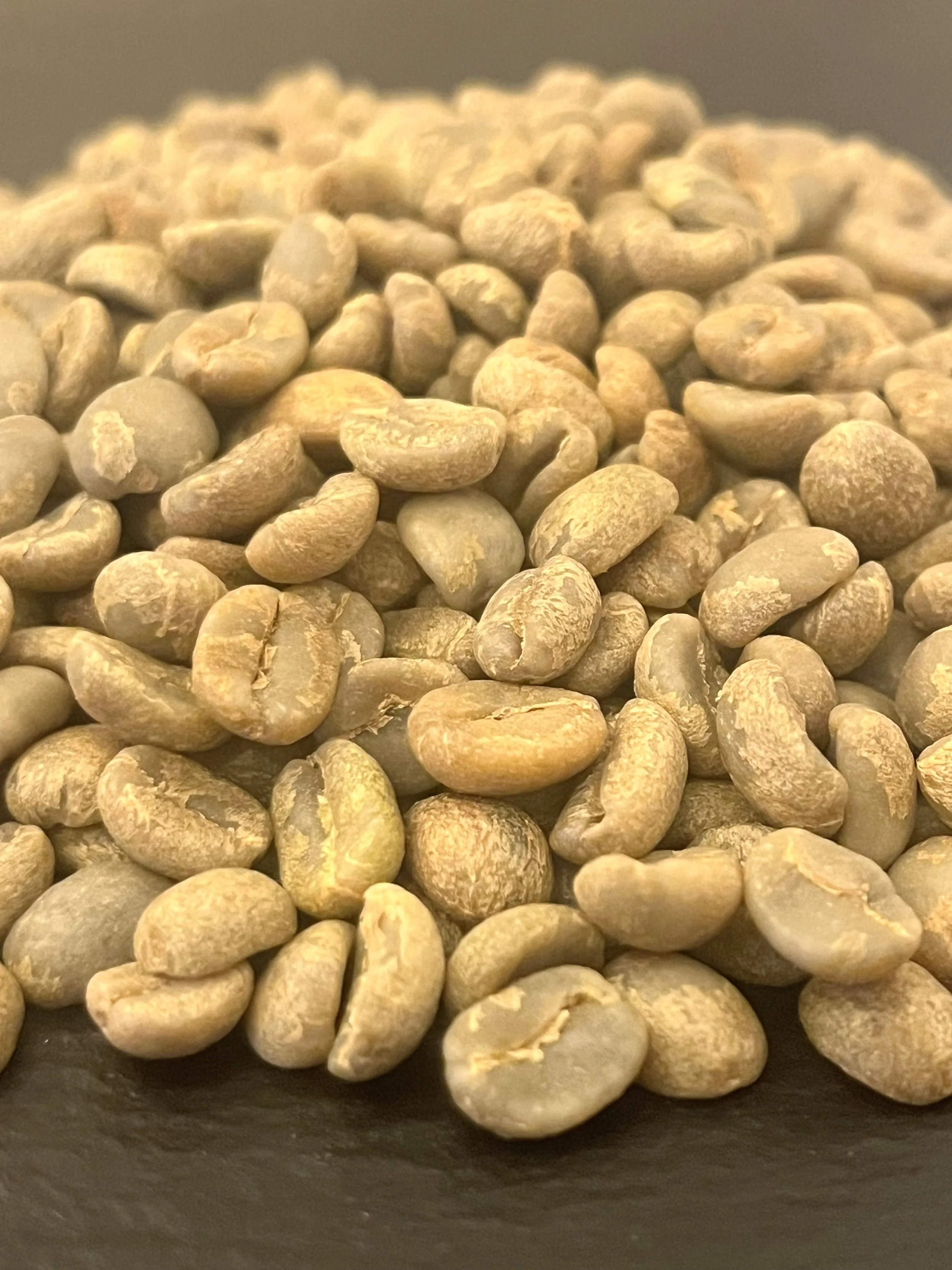 Close-up of green coffee beans on dark surface.