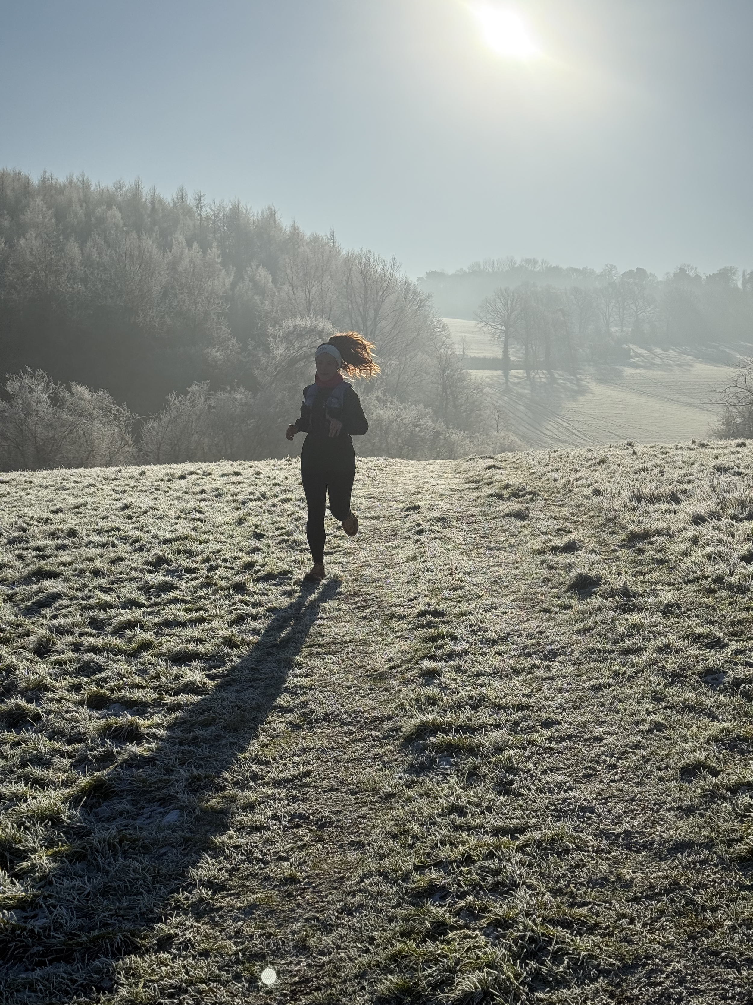 Person running outdoors on a frosty morning trail, with a backdrop of frosted trees and hills under a bright sun.