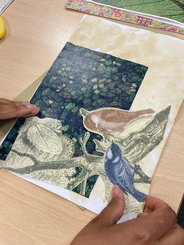 Two hands holding collage sheets, one with birds and a tree, another with a forest scene.