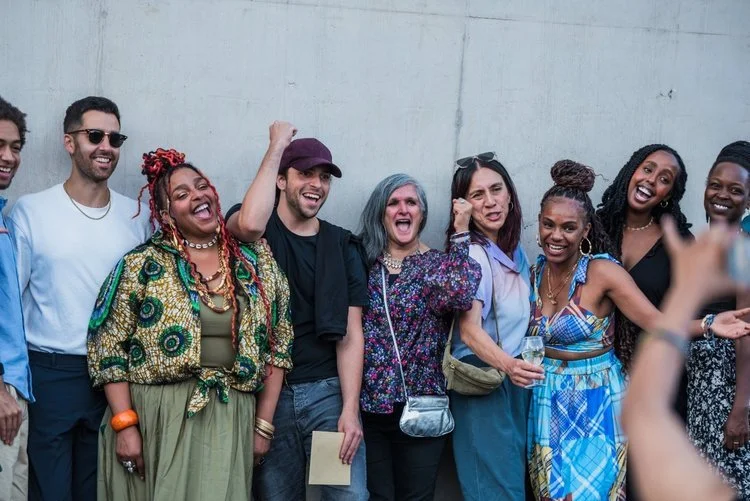 A diverse group of people smiling and laughing together at an outdoor gathering.
