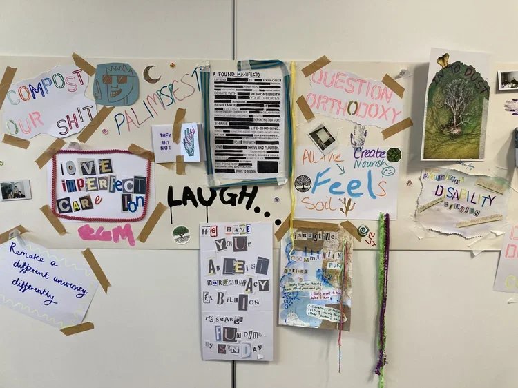 A collection of various colorful posters, drawings, and notes taped to a white wall or board. The signs include words like "Laugh," "Love imperfect care," "Create," and phrases about self-awareness and community, with decorative elements like drawing