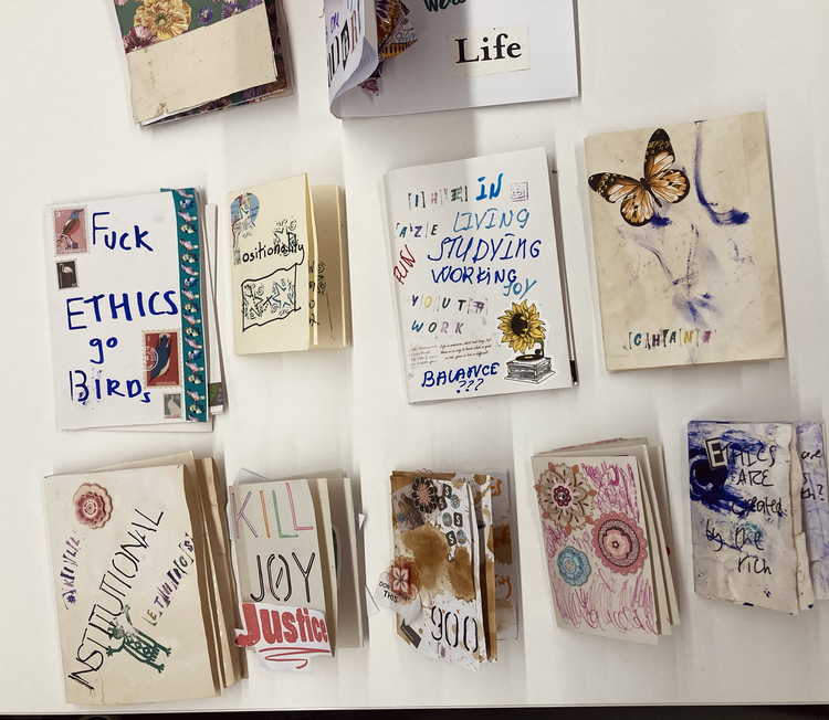 Collage of various handmade paper artworks, including colorful drawings, handwritten words like 'Justice,' 'Joy,' 'Ethics,' 'Birds,' and 'Life,' and illustrations of a butterfly, flowers, a sunflower, and abstract designs, arranged in overlapping and