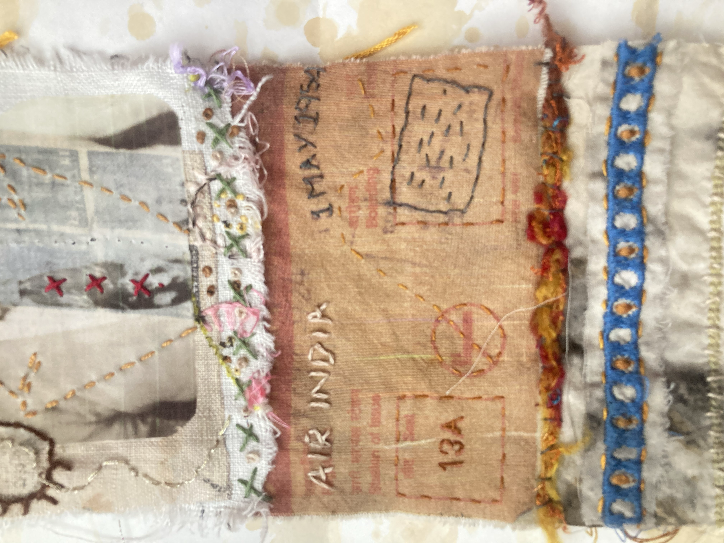 Close-up of a piece of fabric art with embroidered and stitched details, featuring a newspaper clipping, colorful threads, and intricate embroidery patterns.