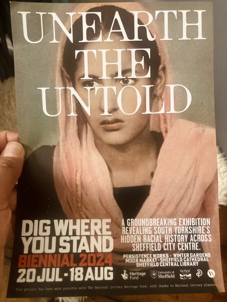 Poster for 'Unearth the Untold' exhibition with a woman wearing a pink headscarf, promoting a South Yorkshire racial history exhibit at Sheffield City Centre from July 20 to August 18, 2024.