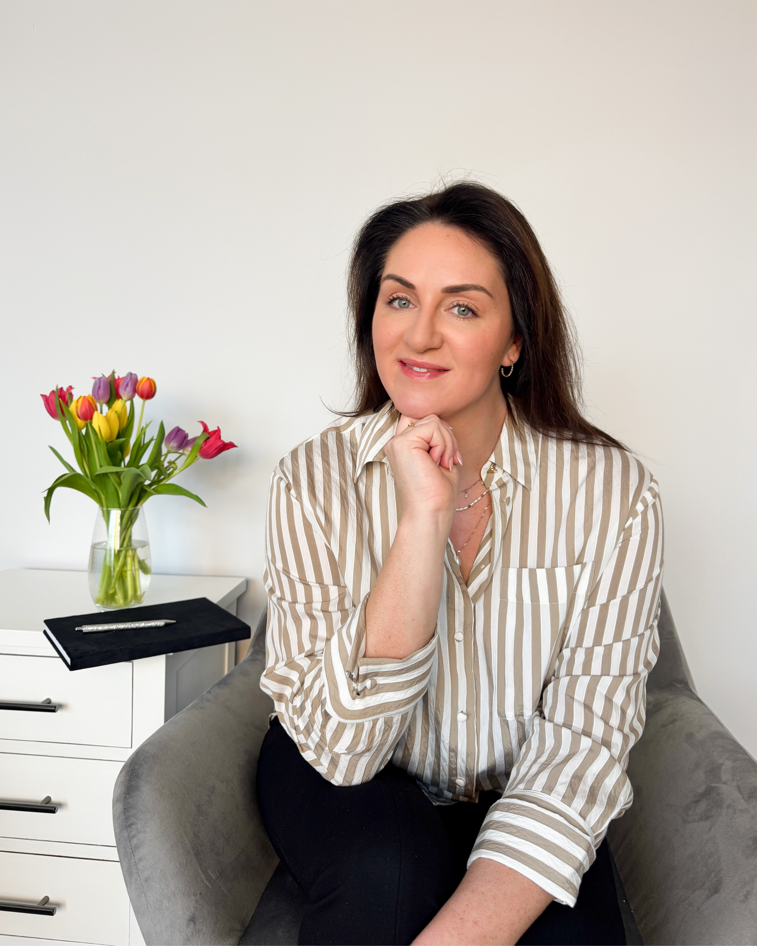 Sarah Precious, Devon wedding celebrant at Sunday Best Ceremonies, seated indoors beside colourful tulips and a notebook.