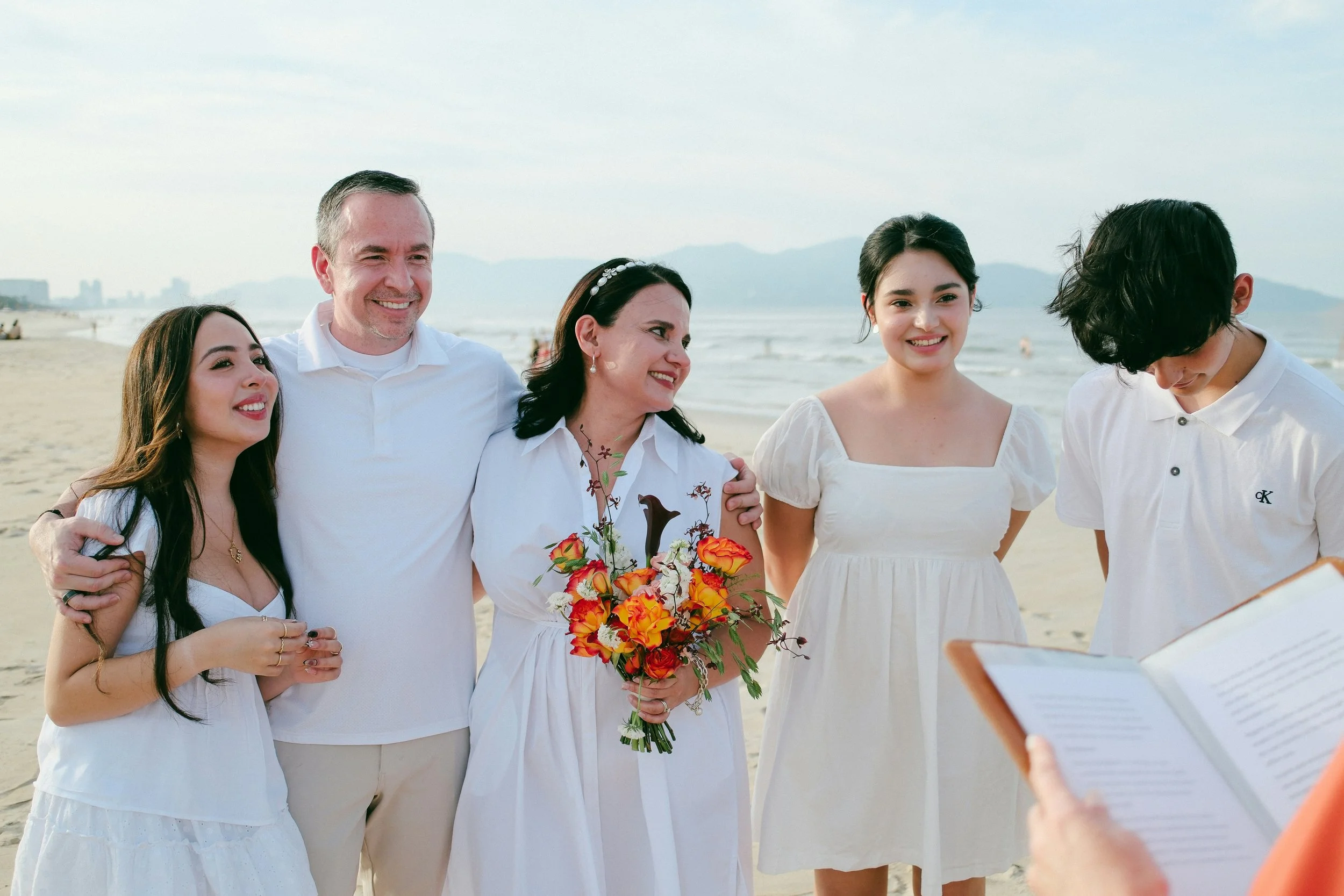 Family vow renewal ceremony on a beach, with a couple and their children standing together during a relaxed seaside celebration.