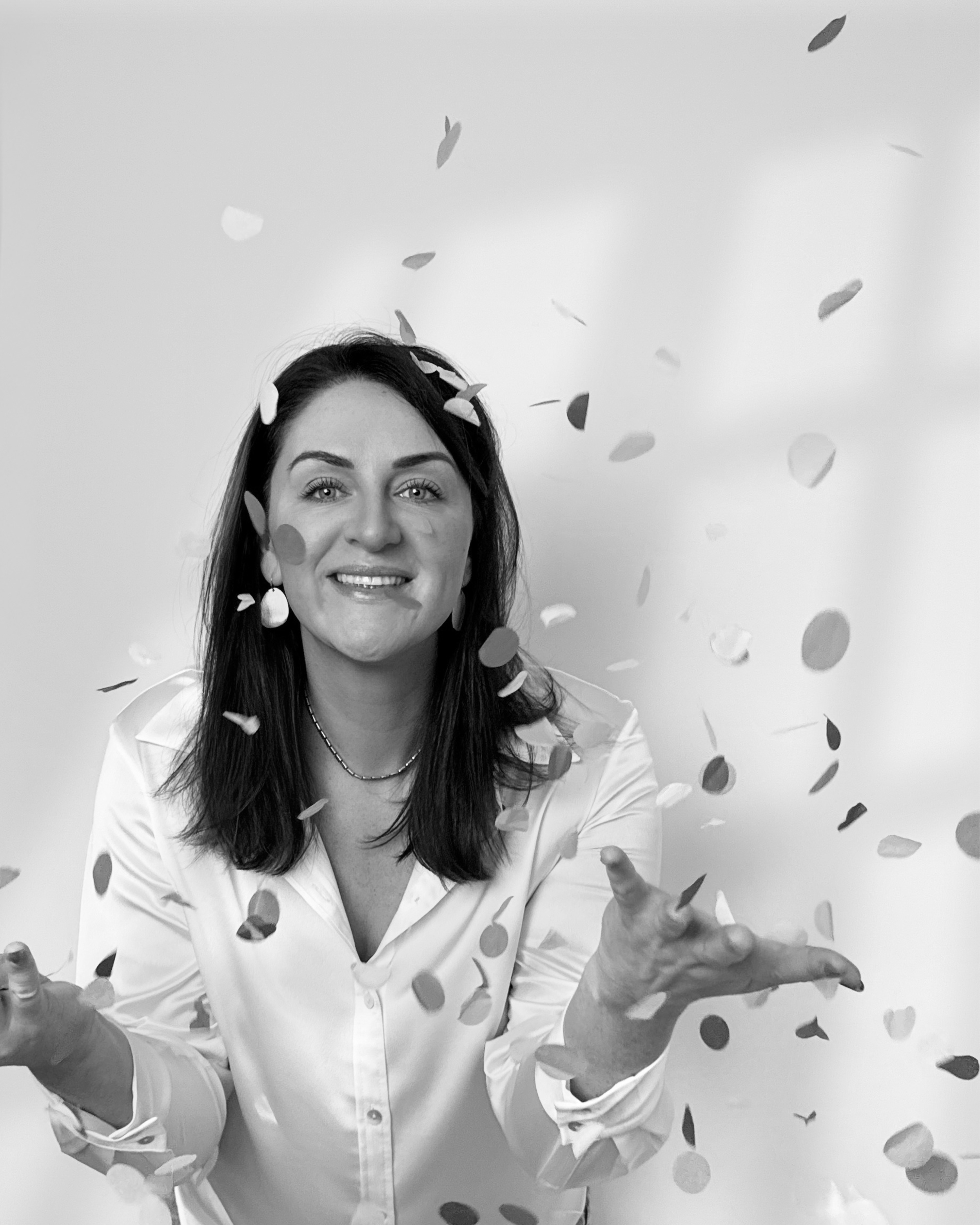 Sarah Precious wedding celebrant from Sunday Best Ceremonies who has dark hair smiling, wearing a white button-up shirt, surrounded by falling confetti.