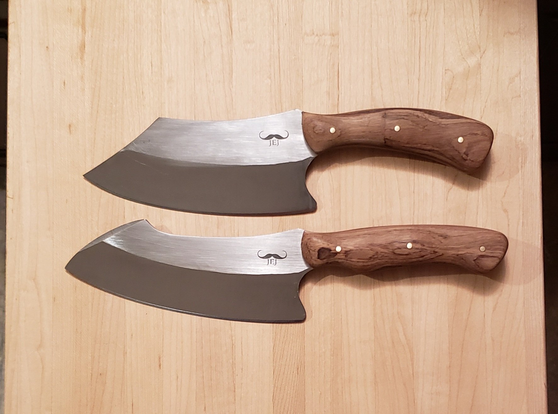Two chef knives with stainless steel blades and wooden handles resting on a wooden surface.
