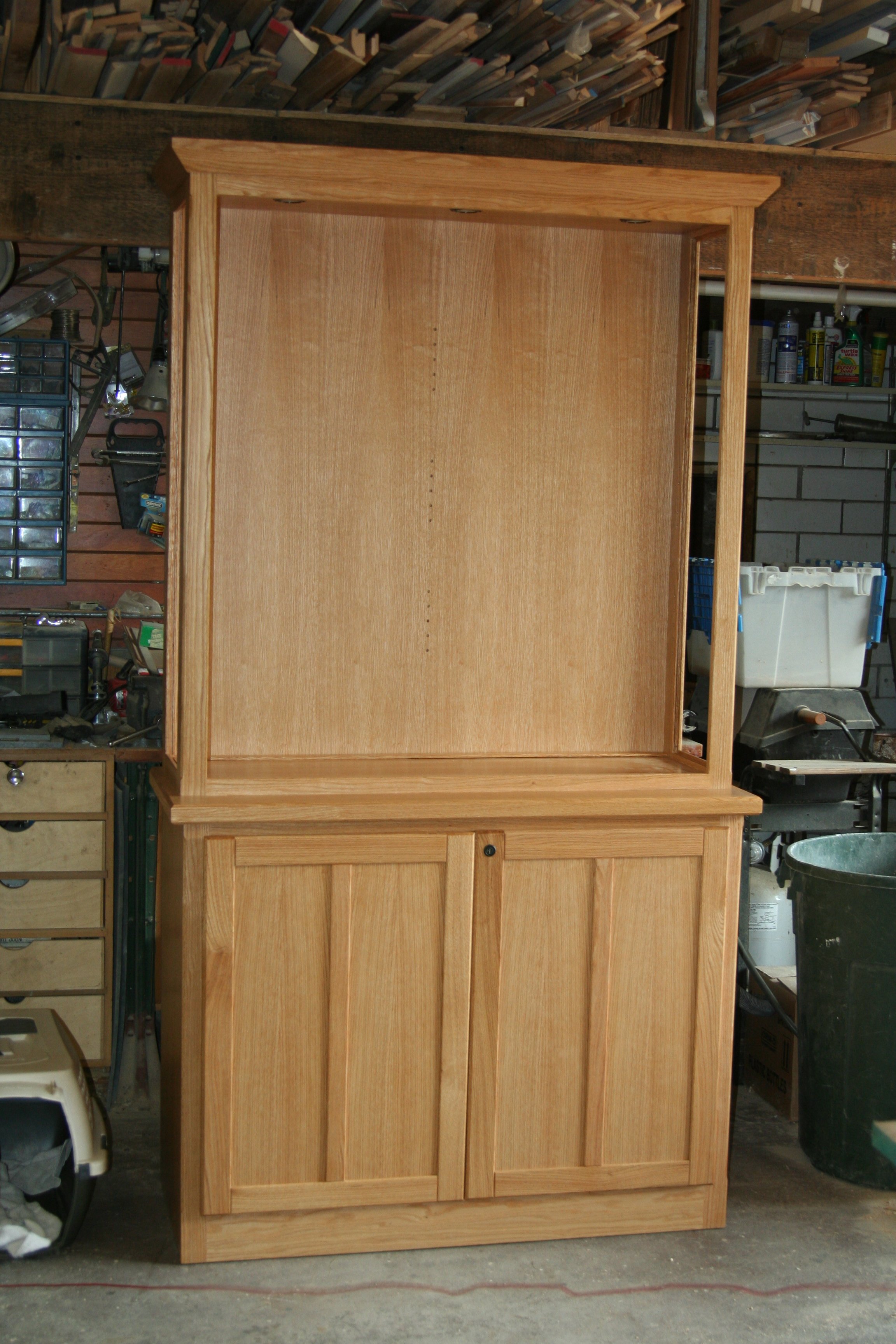 Unfinished wooden cabinet with open upper section and closed lower section with two doors in a garage or workshop.