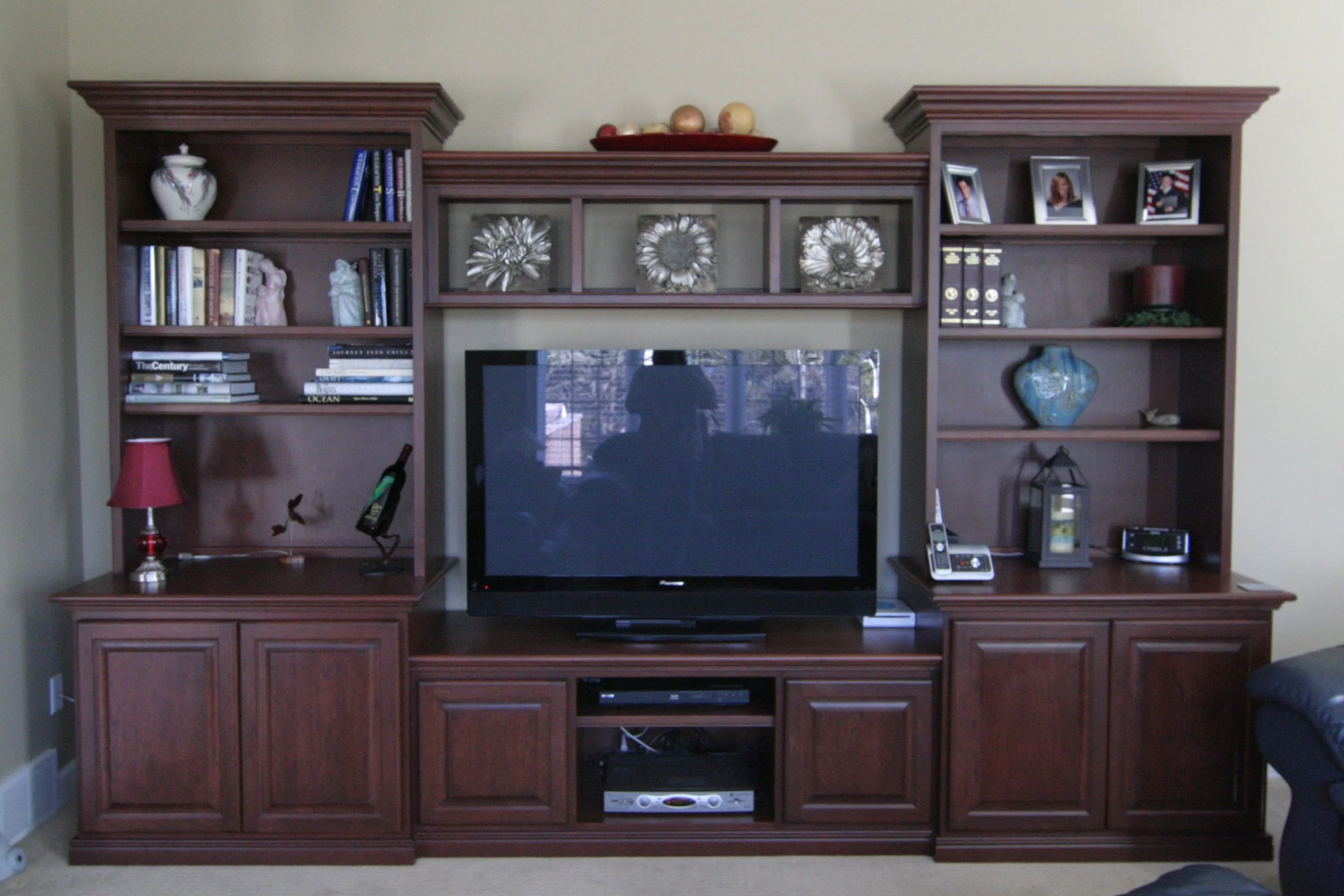 A wooden entertainment center with a flat-screen television in the center, surrounded by shelves holding books, decorative items, and picture frames.