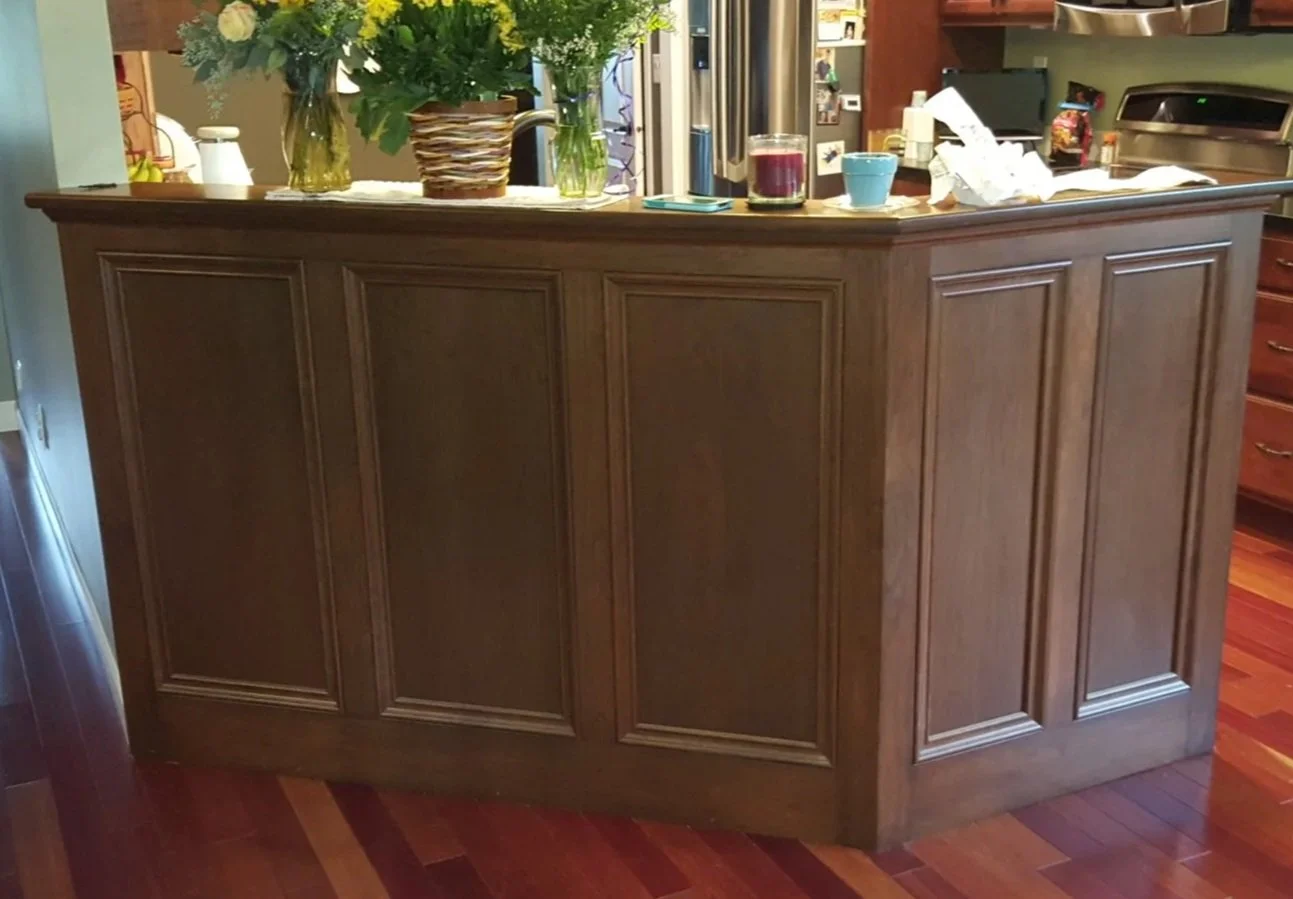 Kitchen island with flowers, candles, bowls, and various items on top, in a kitchen with wooden flooring and cabinetry.