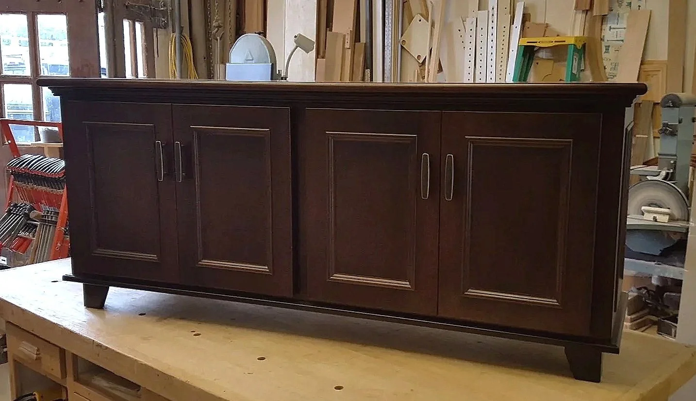 Dark brown wooden sideboard or credenza with four doors and short legs in a woodworking shop.