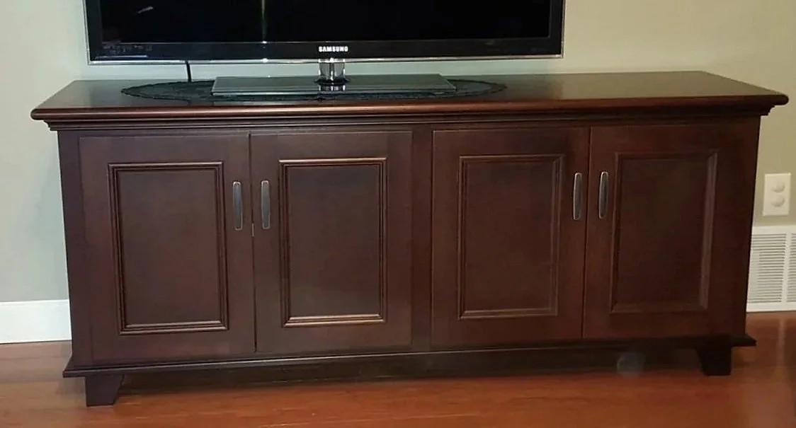 A wooden TV stand with three cabinet doors, holding a flat-screen television on top, in a room with hardwood floor.