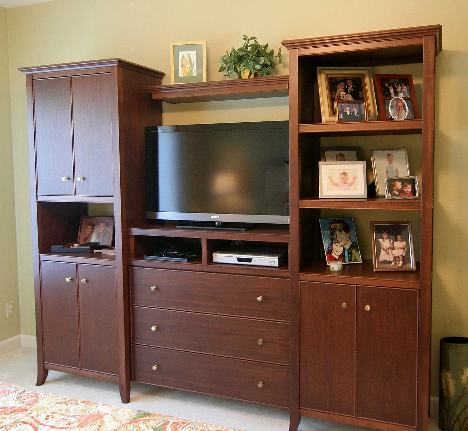Wooden entertainment center with a TV, framed photographs of family members, and decorative items on top.