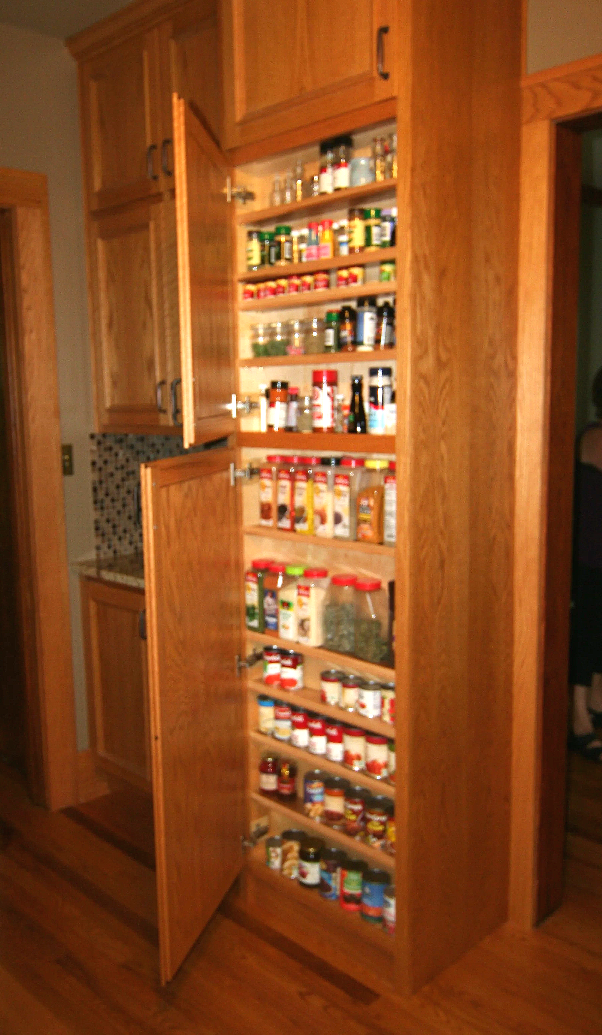 Open wooden pantry cabinet filled with various spices, herbs, and seasonings stored in jars and bottles.